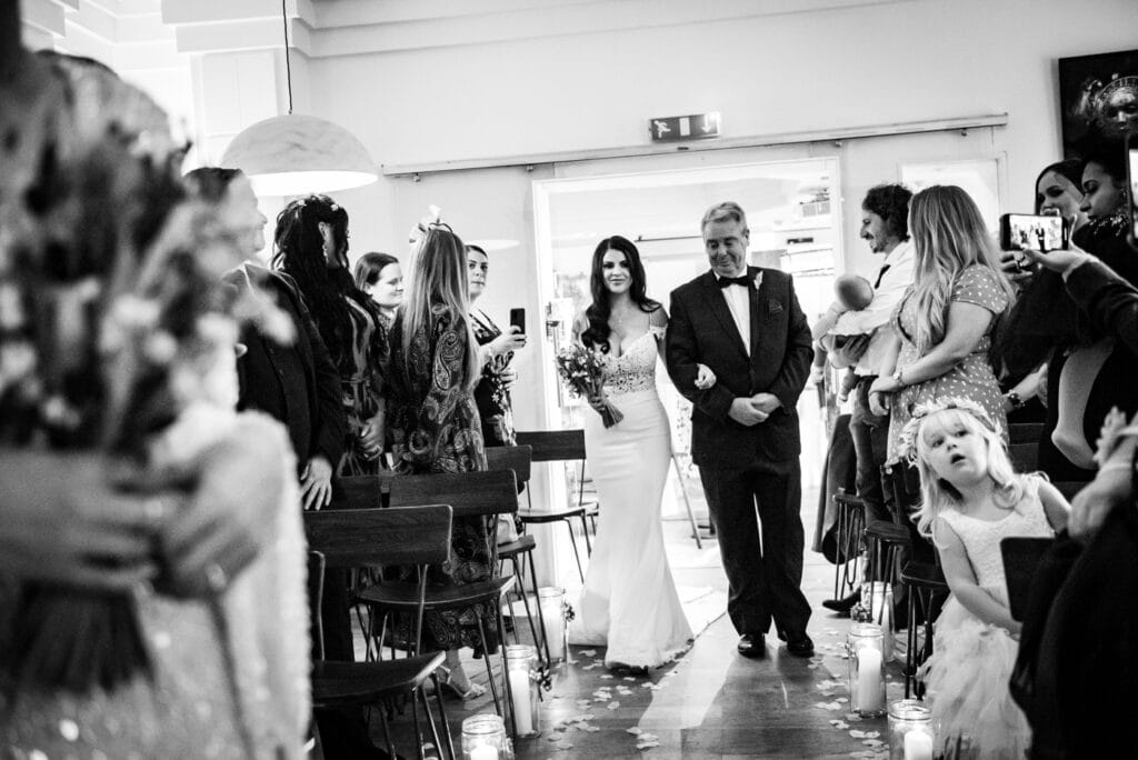 bride is walking down the aisle with her dad at the square club bristol wedding