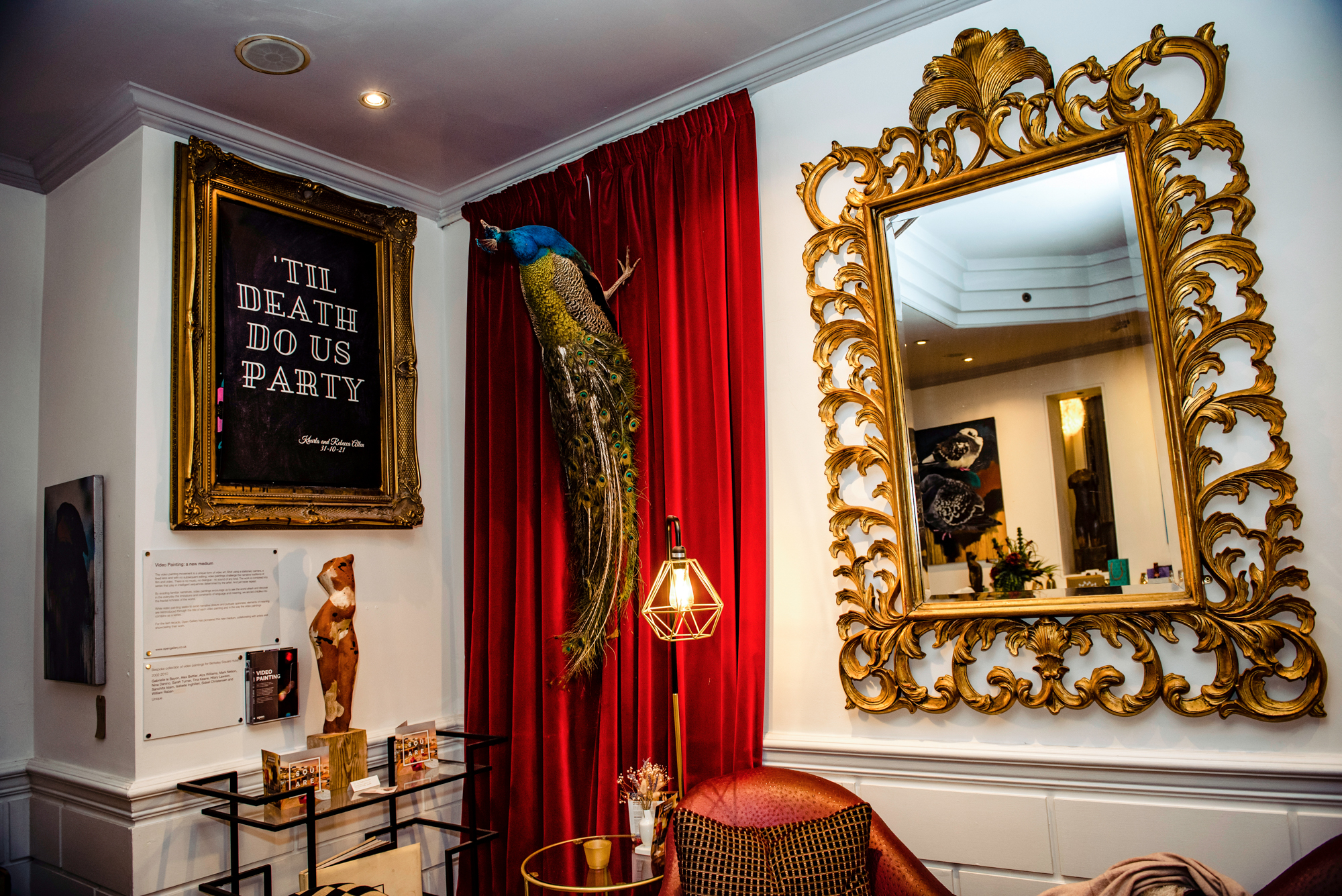 Interior of The Square Club Bristol with gold-framed mirrors, red velvet drapes, and quirky art details.
