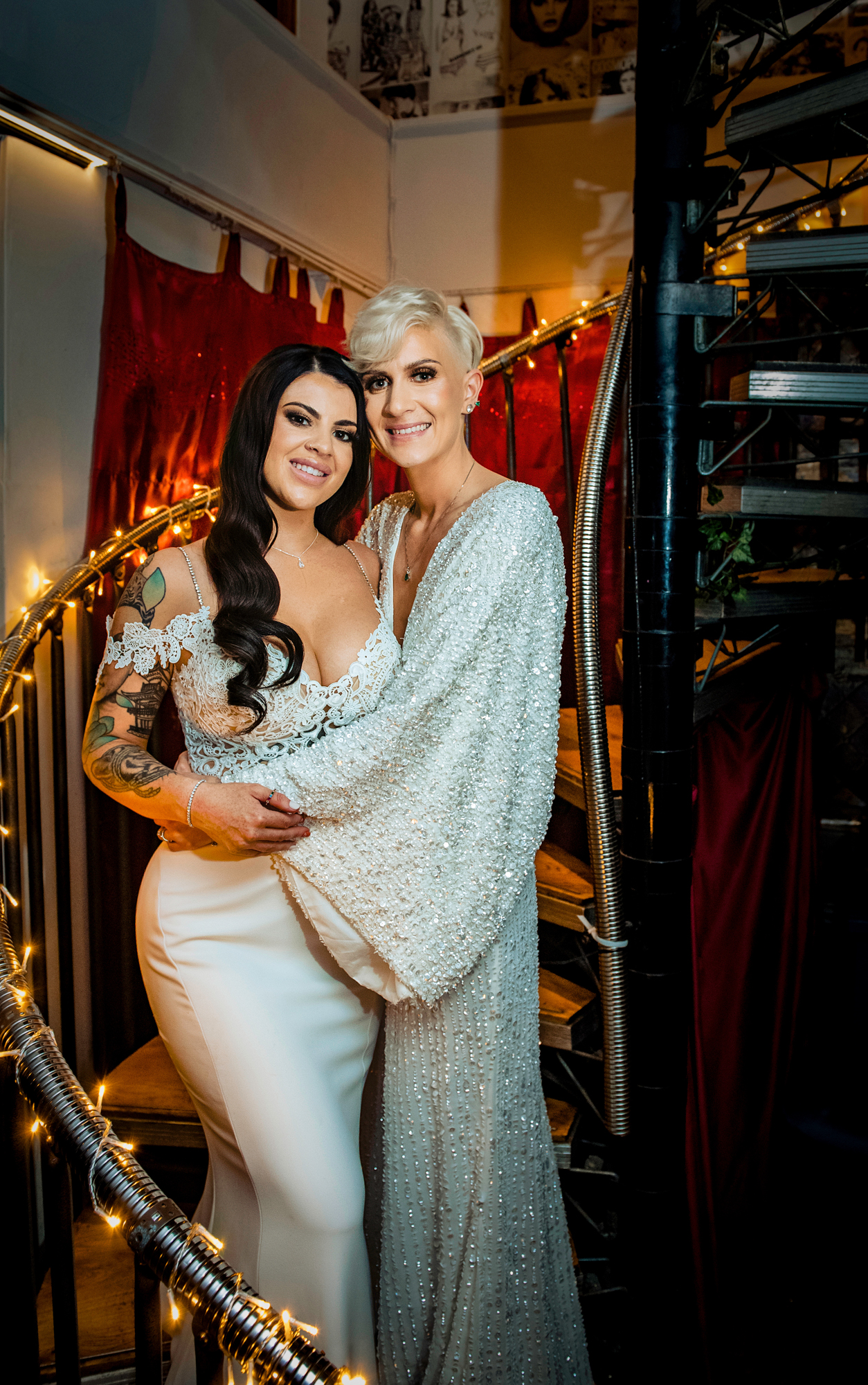 Romantic portrait of two brides embracing on the spiral staircase wrapped in fairy lights at The Square Club Bristol.