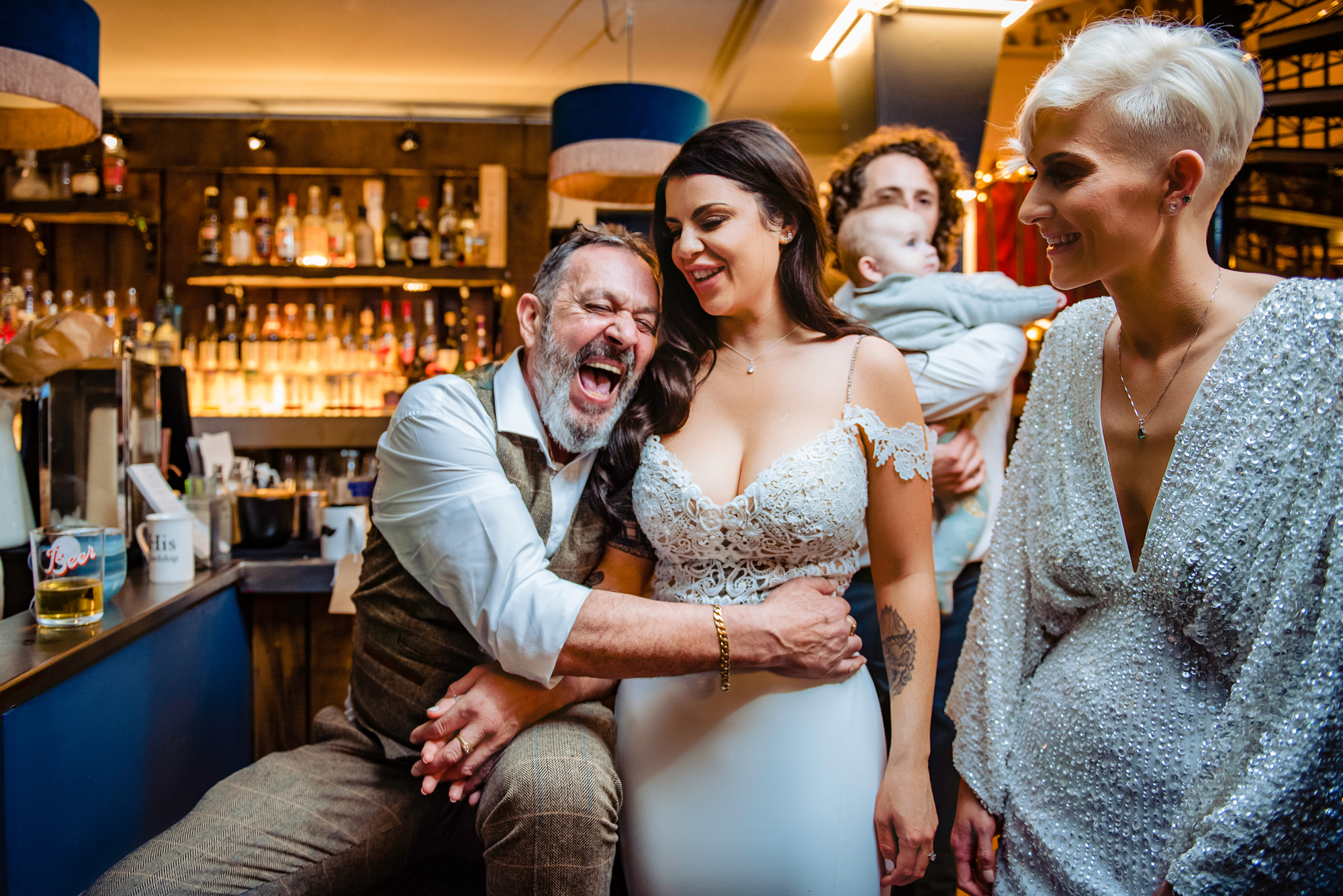 Candid moment of laughter at the bar between the brides and guests during a lively wedding.