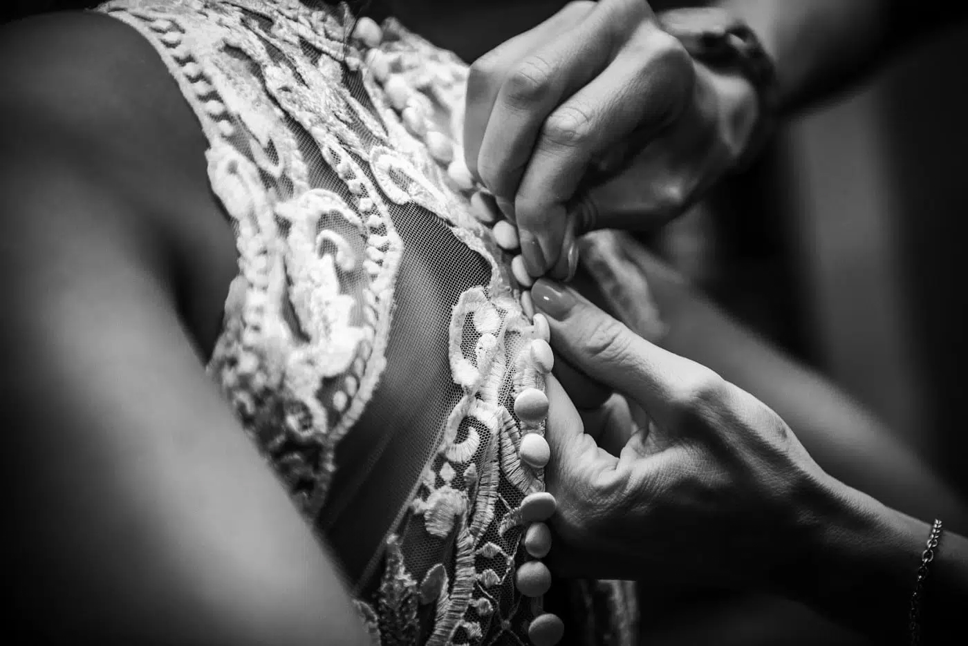 Close-up of hands fastening lace wedding dress buttons during bridal preparations.