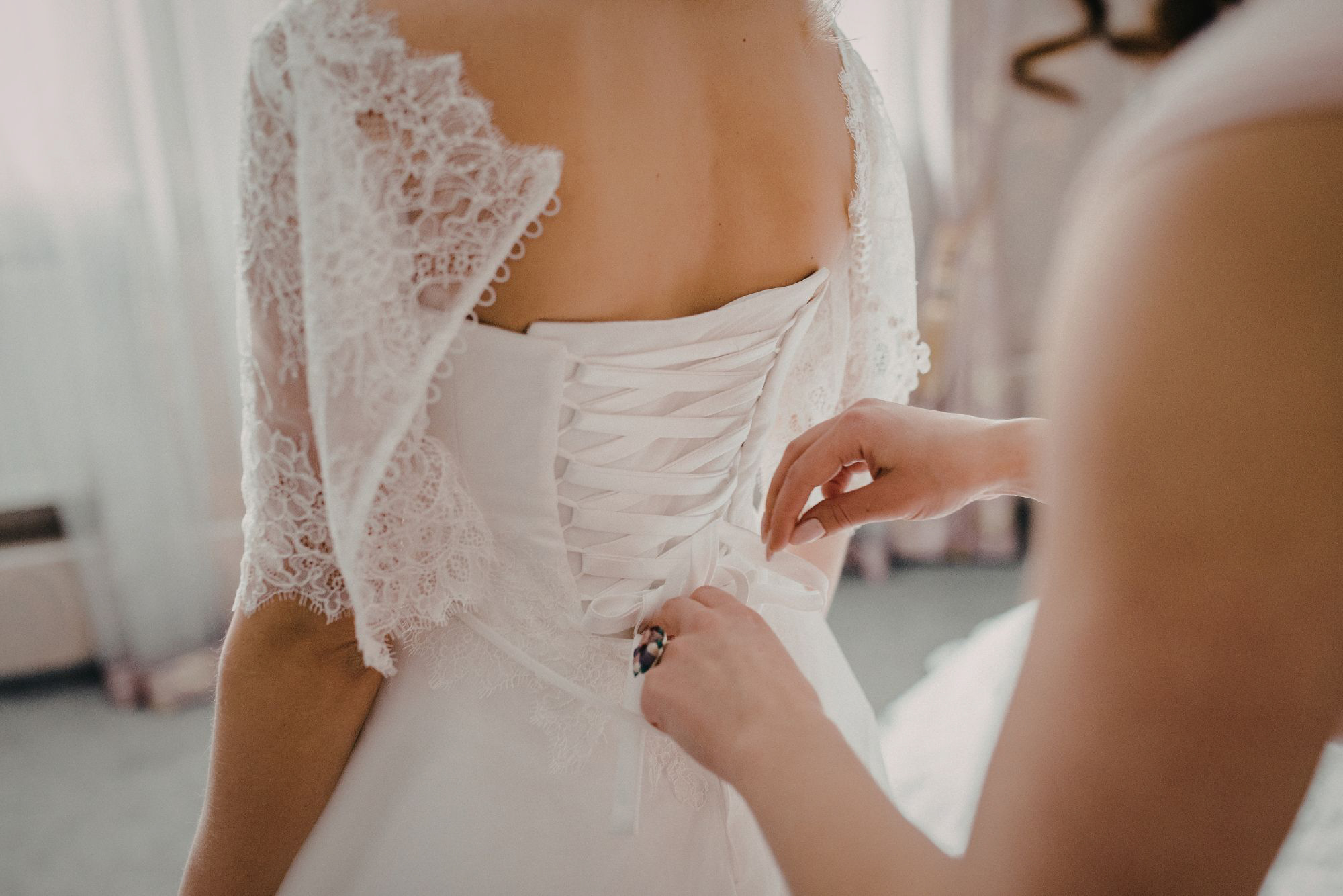 Hands tying corset back of wedding dress during bridal preparations before ceremony.