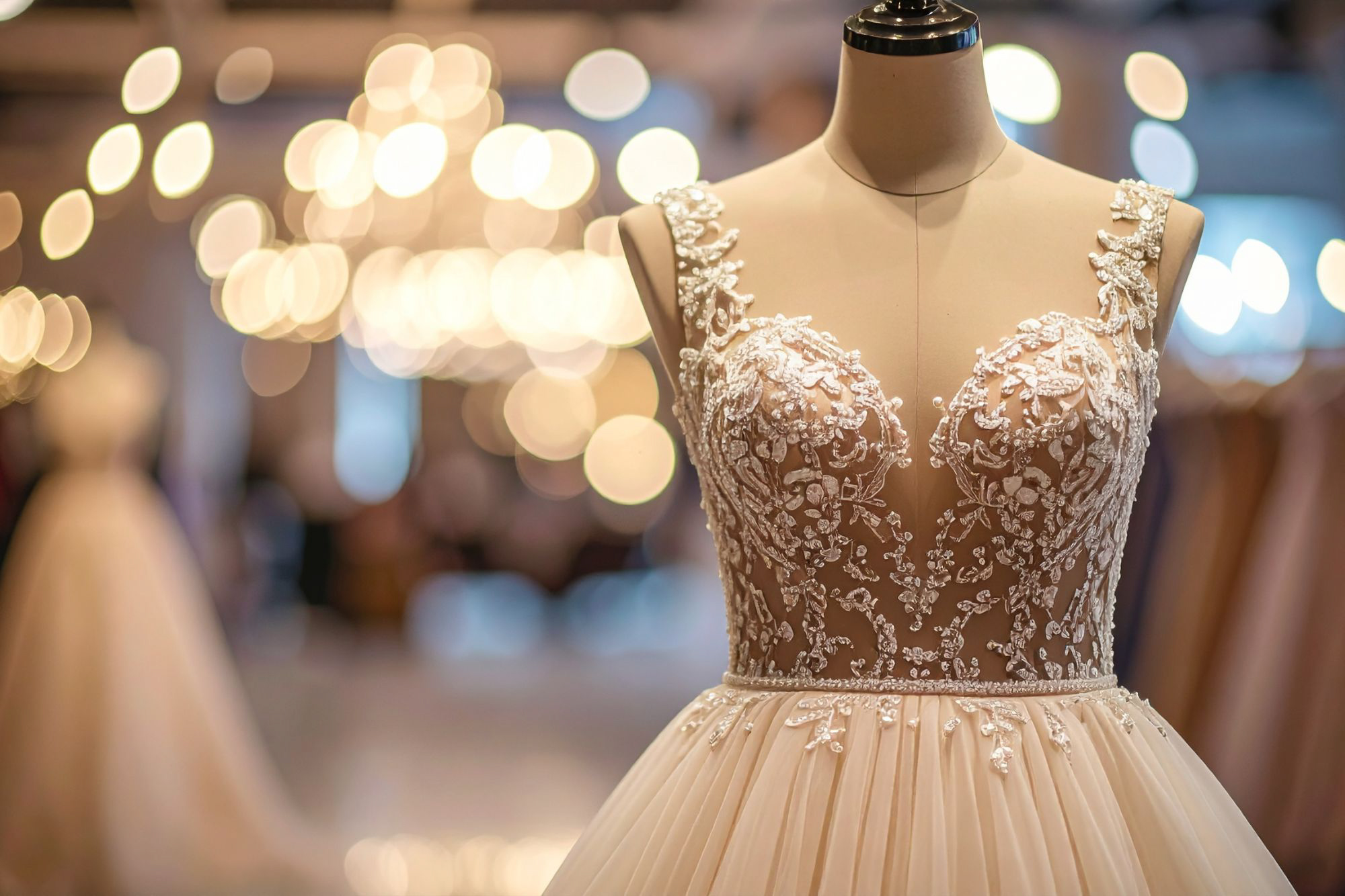 Beaded wedding dress displayed on mannequin with warm lights creating elegant bridal boutique atmosphere.