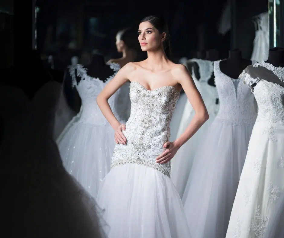 Bride standing among wedding dresses inside bridal boutique while choosing her dream gown.
