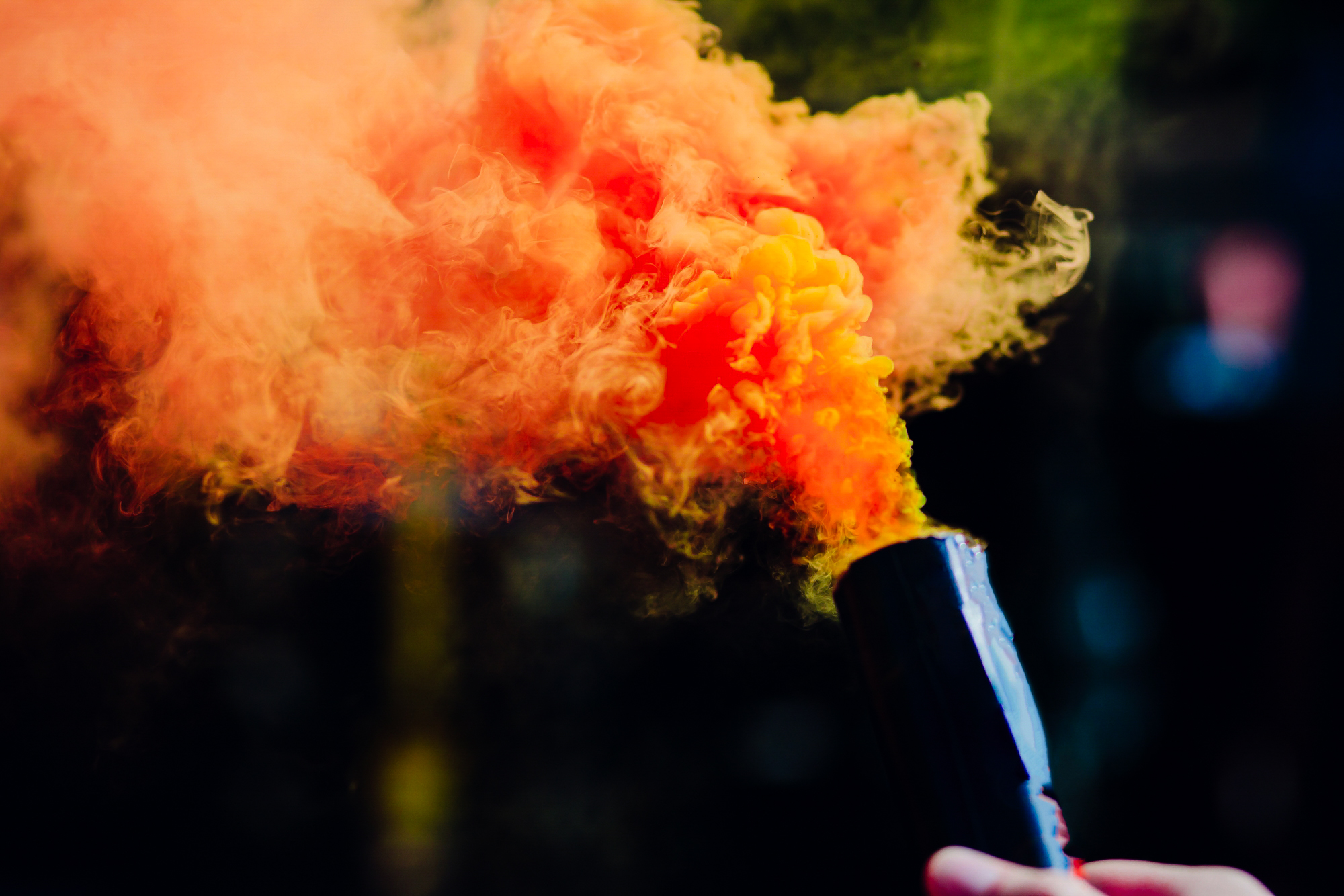 Close-up of an orange smoke bomb with swirling colour against a dark blurred background.