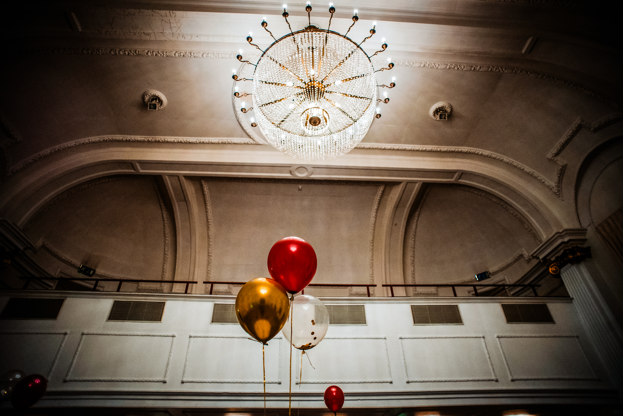 Red, gold, and clear balloons beneath chandelier at Bristol Grand Hotel gala dinner venue.