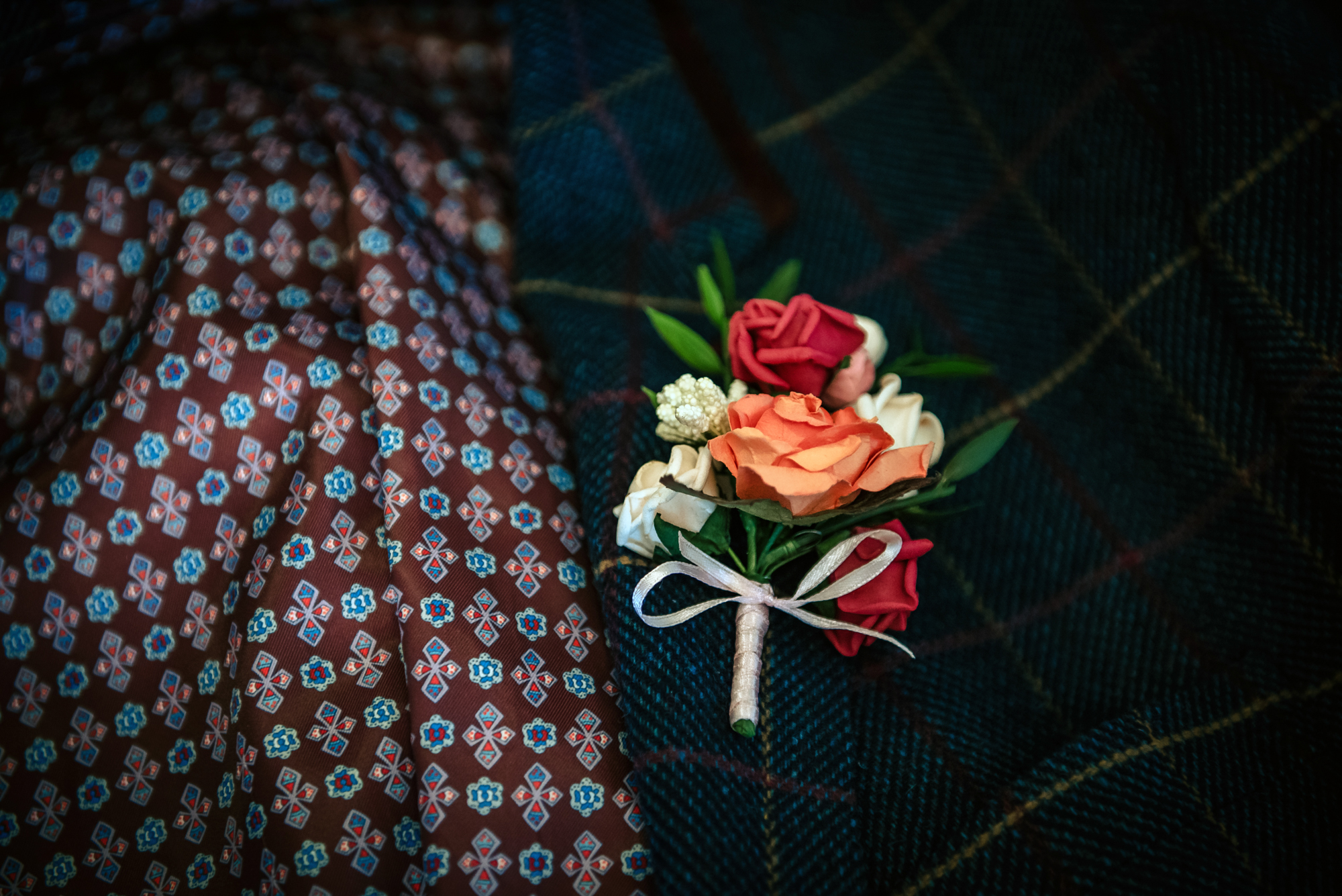 A colourful buttonhole rests on checked fabric, echoing traditional Scottish tones and textures.
