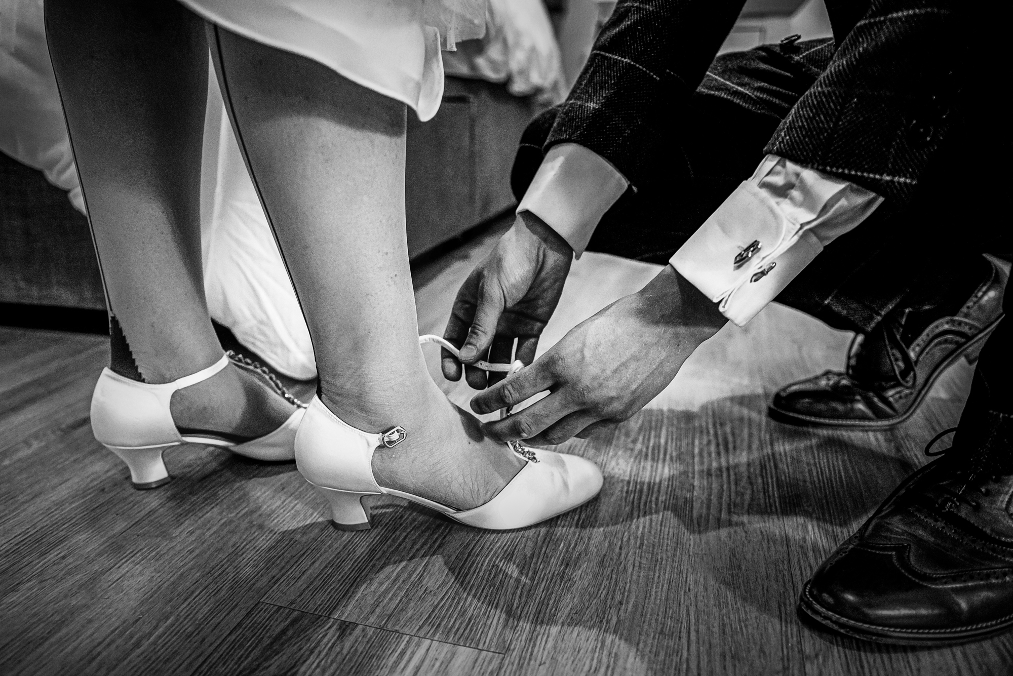 The bride's son kneels to fasten the bride’s shoes, capturing a quiet, tender pre-ceremony moment.