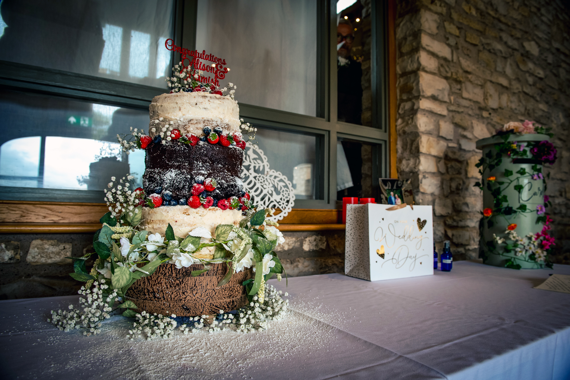 A tall rustic wedding cake decorated with berries and flowers sits ready for the celebration.