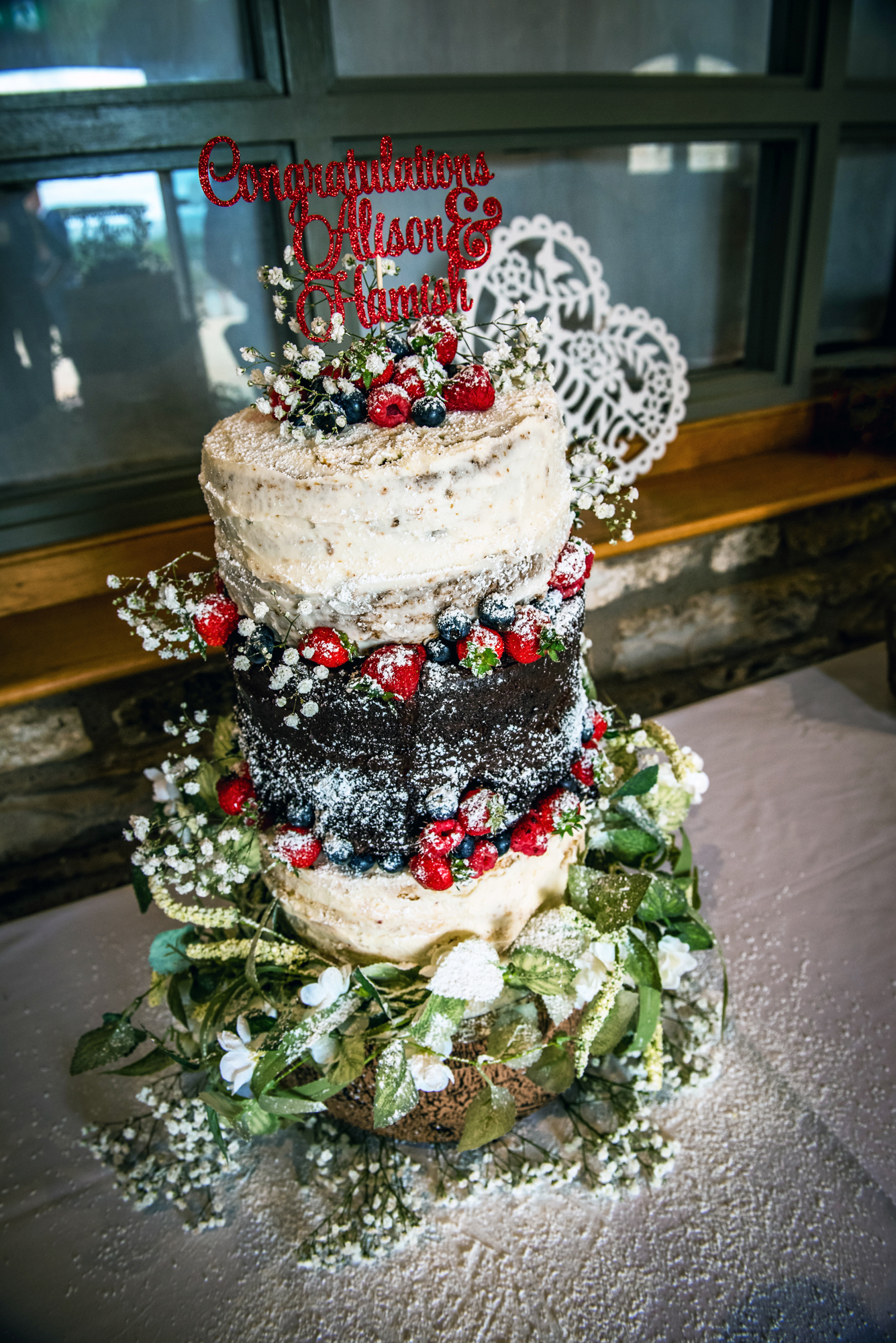 The wedding cake topper sits above layers of berries and icing, dusted with powdered sugar.