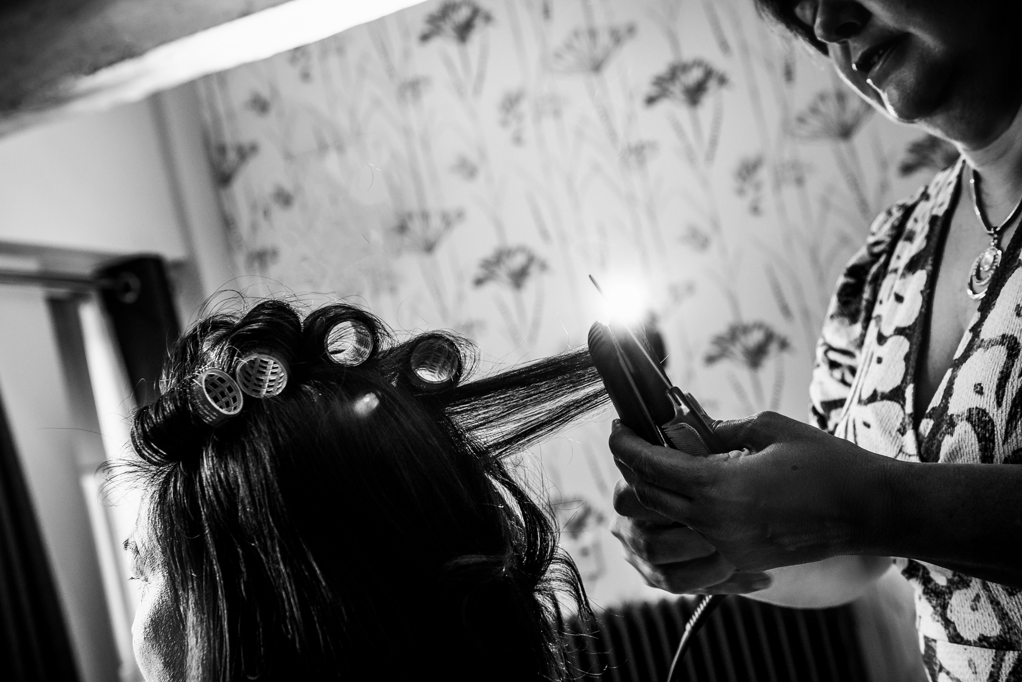 The bride's hair is curled and straightened during morning preparations, with soft light catching the steam.