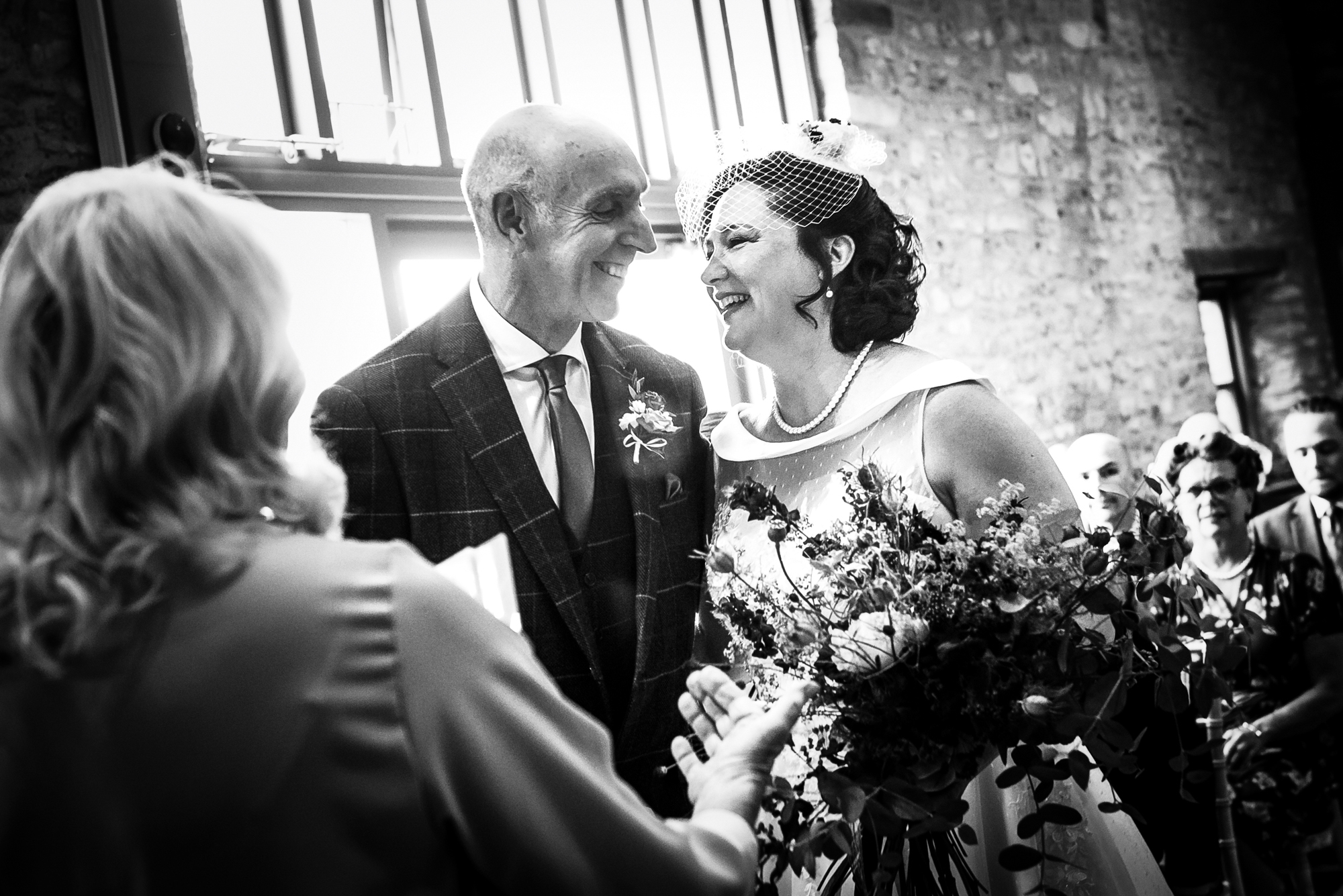 The bride smiles warmly at the celebrant while standing beside her partner as guests watch behind them.