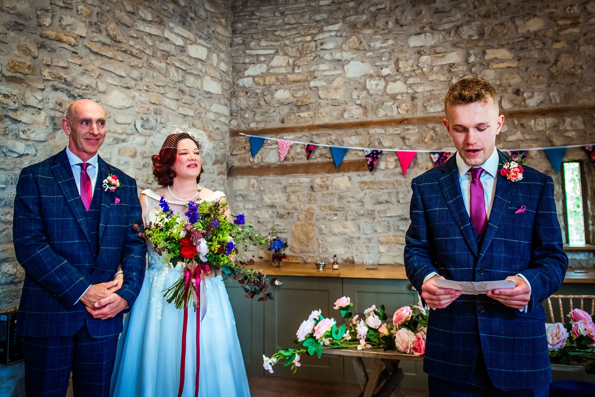 The couple stands smiling with their bouquets while their son reads aloud during the ceremony.