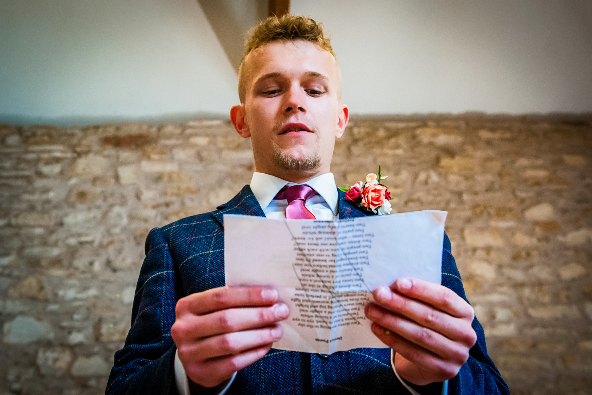 The son reads from a folded page while wearing a blue checked suit and pink tie.
