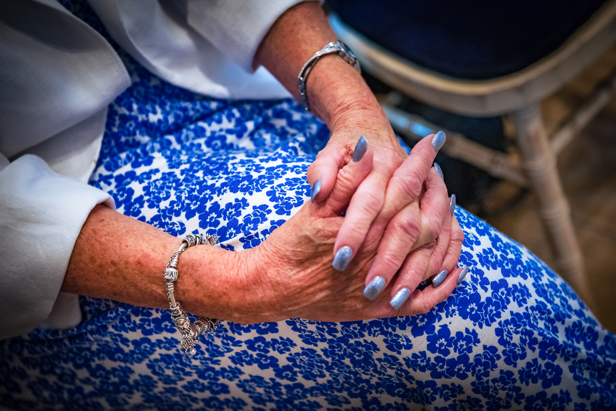 A guest’s hands rest together over a blue floral dress, silver bracelet and nails catching the light.