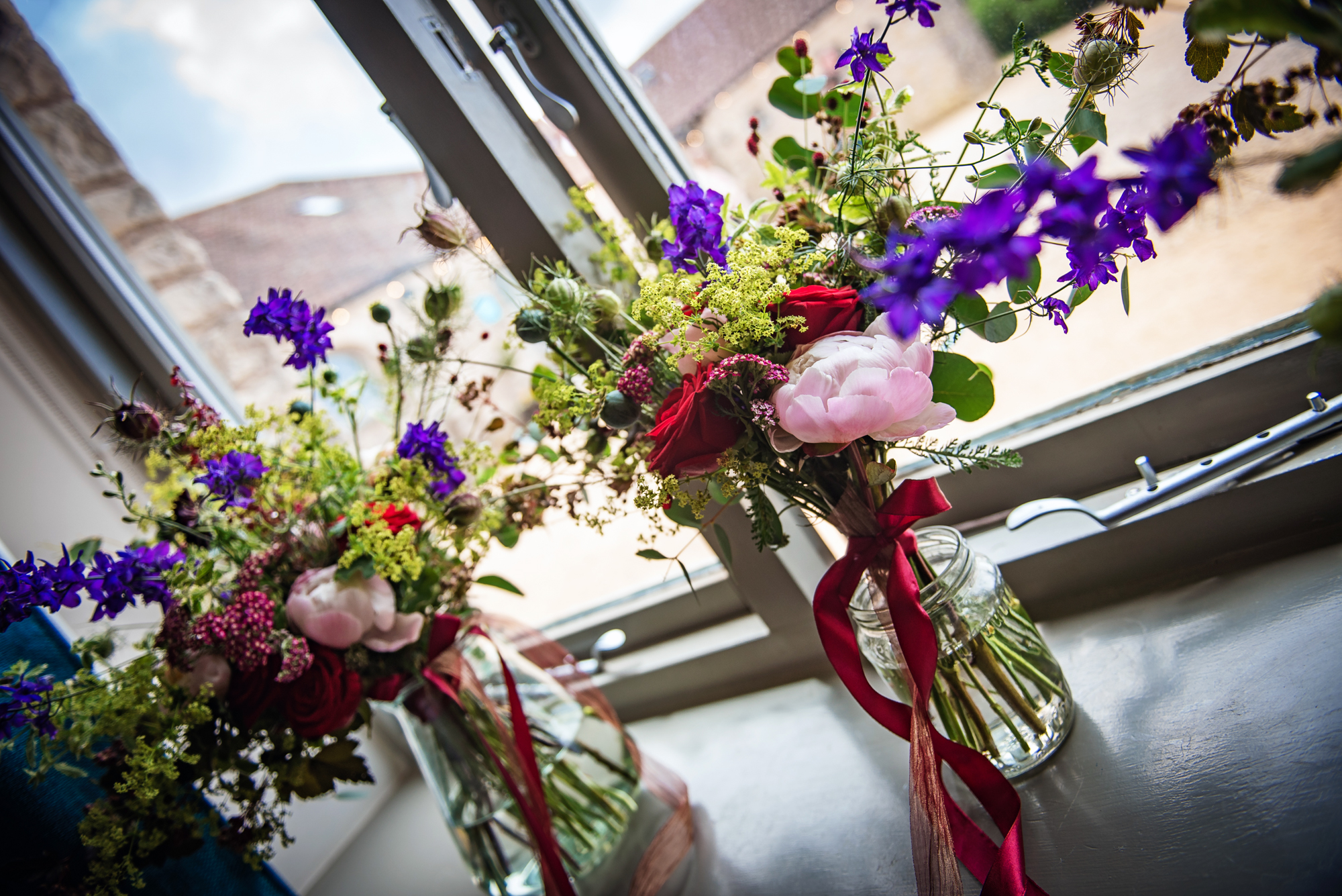 Two wild, colourful bouquets rest on the windowsill, featuring red roses and Scottish-inspired greenery.