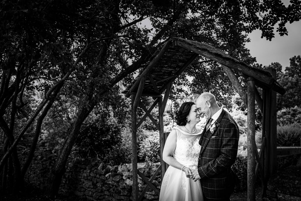 The couple gently touches foreheads beneath the wooden archway.