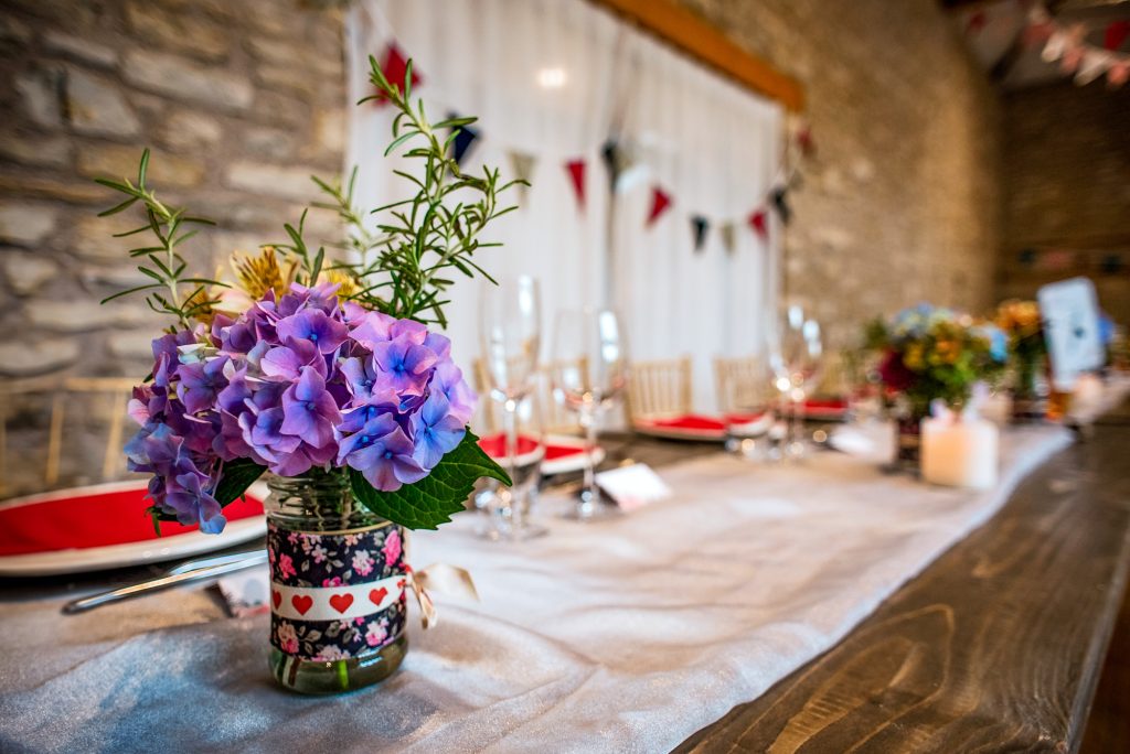 Purple hydrangeas and rosemary sprigs sit in a patterned jar along the wooden top table.
