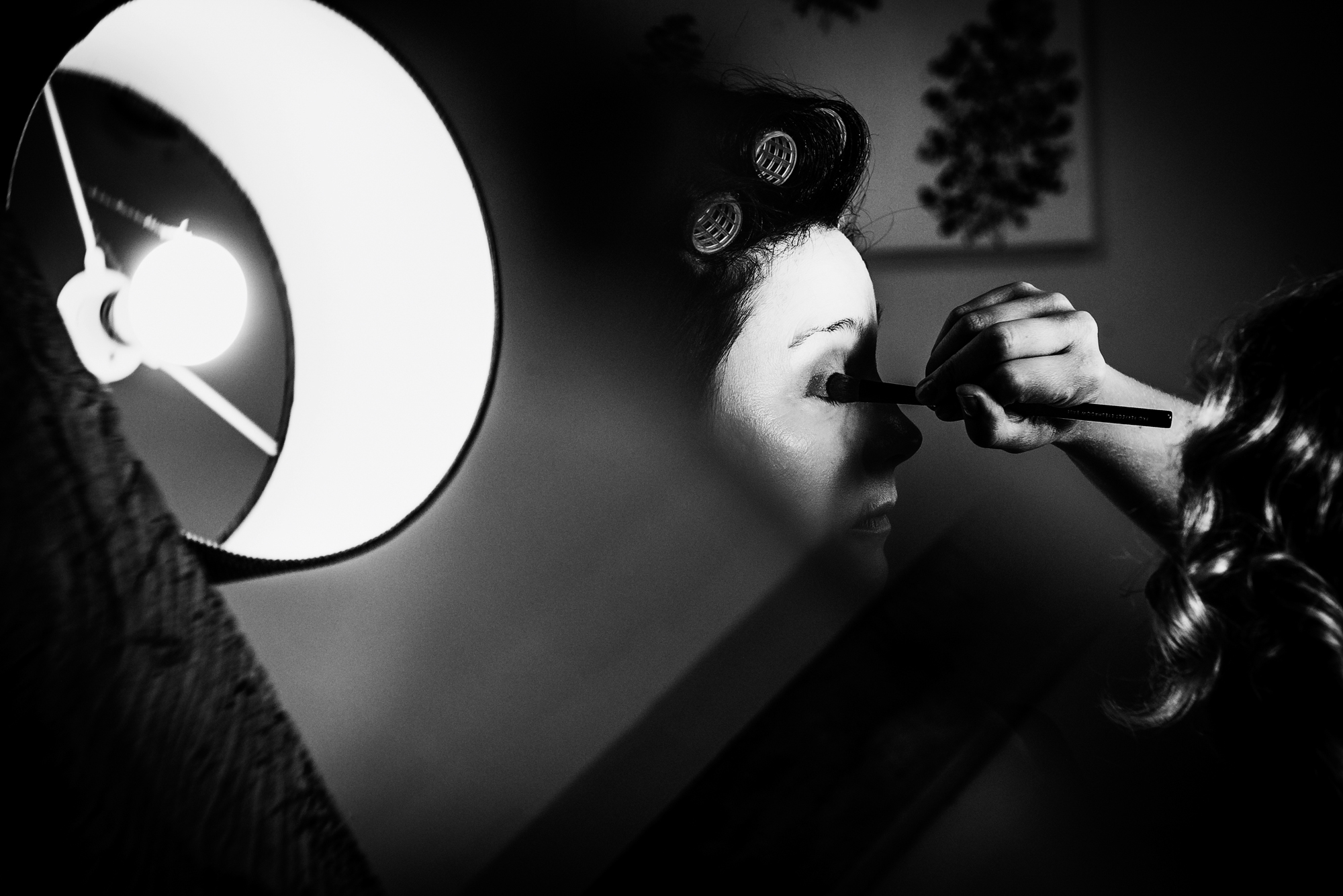 A makeup artist blends eyeshadow under a bright lamp, creating dramatic contrast during bridal preparations.
