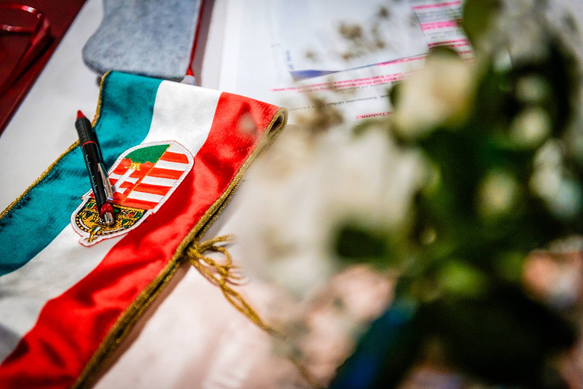 Hungarian ceremonial ribbon and documents displayed on wedding table beside soft floral arrangement.