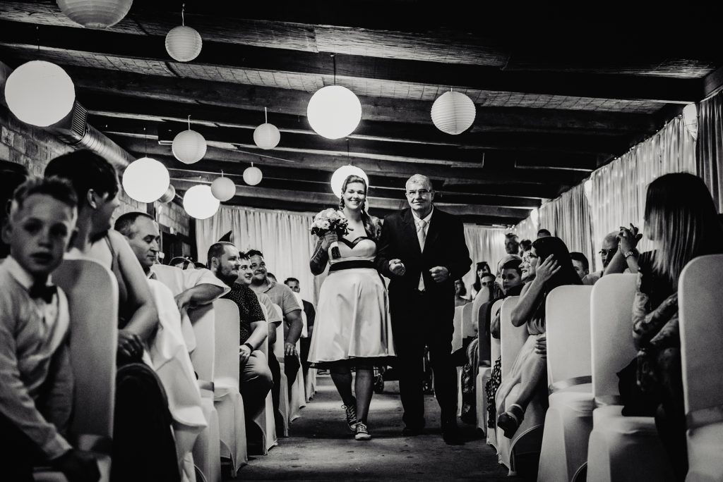 Bride walking down aisle with her father during alternative indoor wedding ceremony in Budapest.
