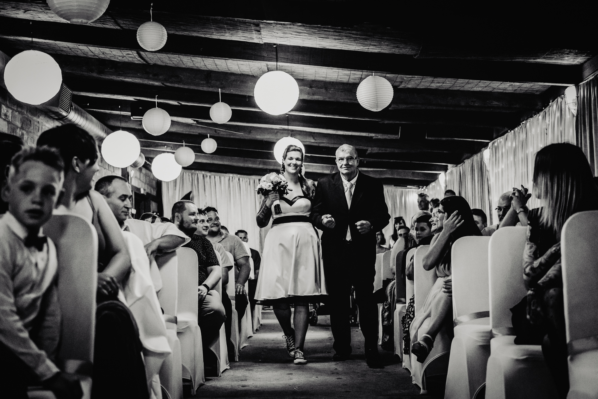 Bride walking down aisle with her father during alternative indoor wedding ceremony in Budapest.