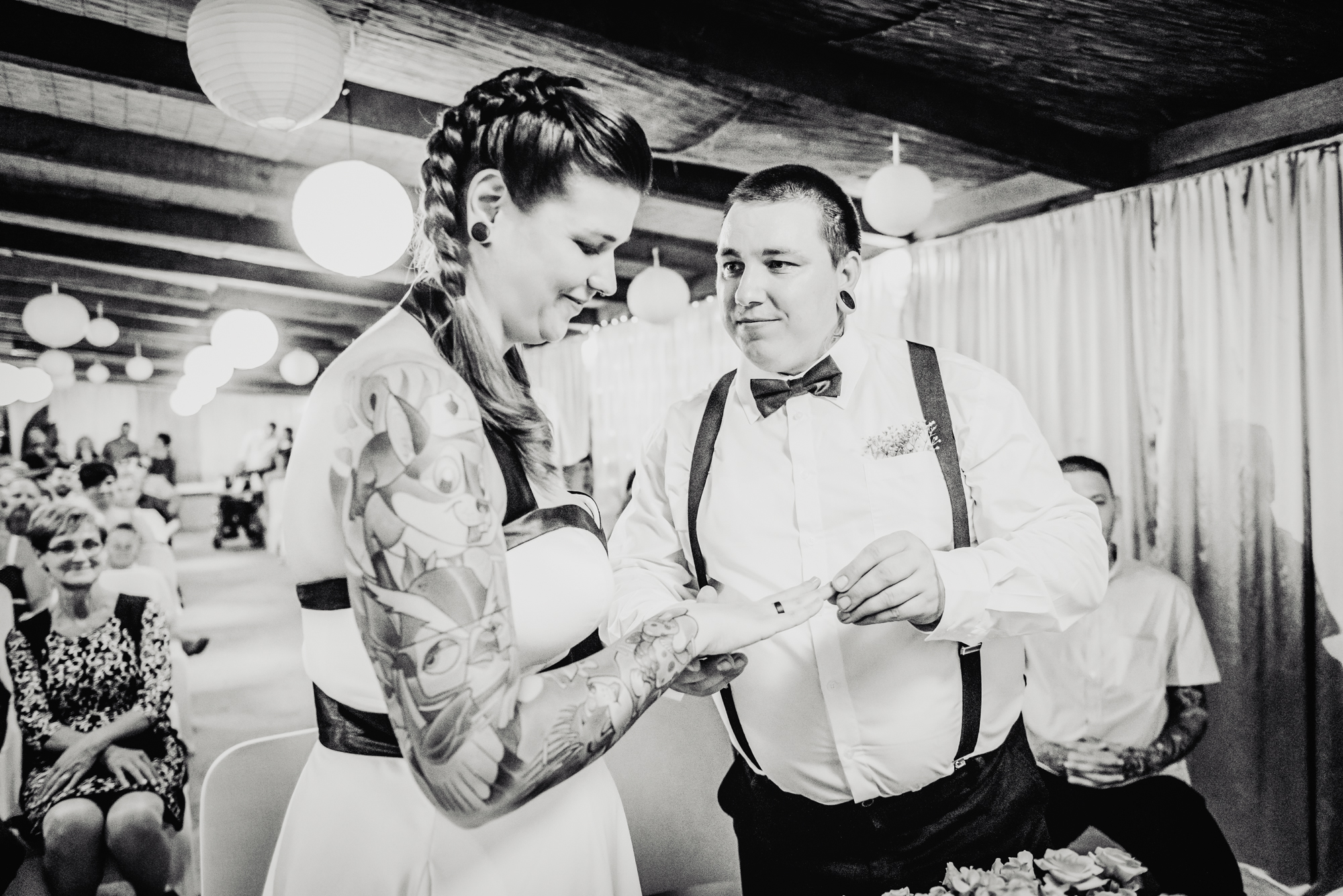 Groom placing wedding ring on bride’s finger during black and white alternative wedding ceremony photograph.