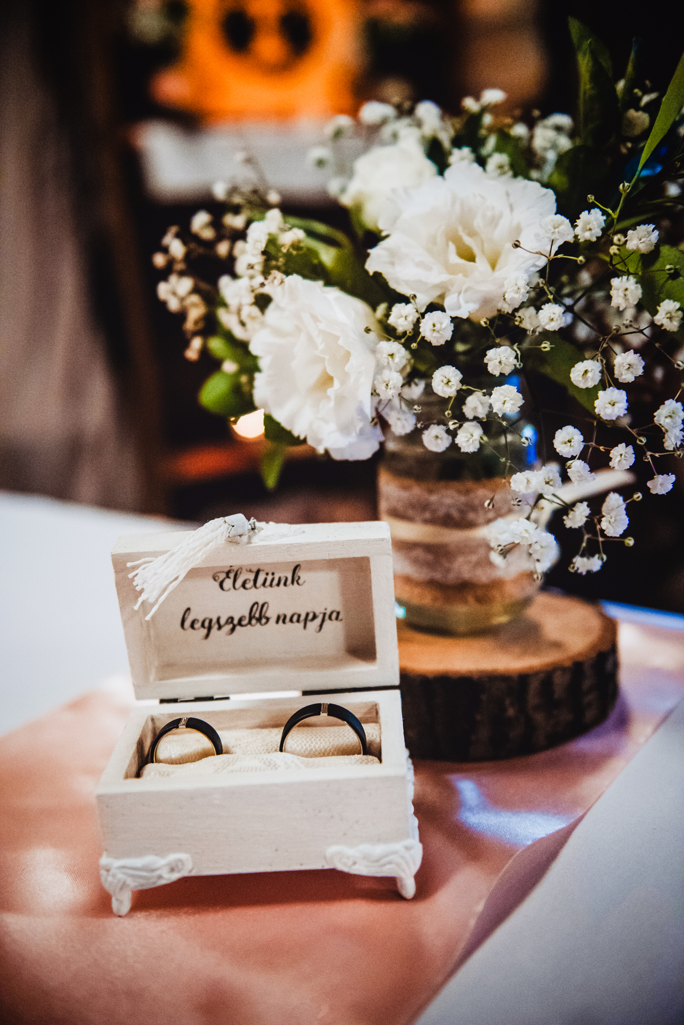 Wedding rings in a wooden ring box beside white flowers during an alternative Budapest wedding reception.
