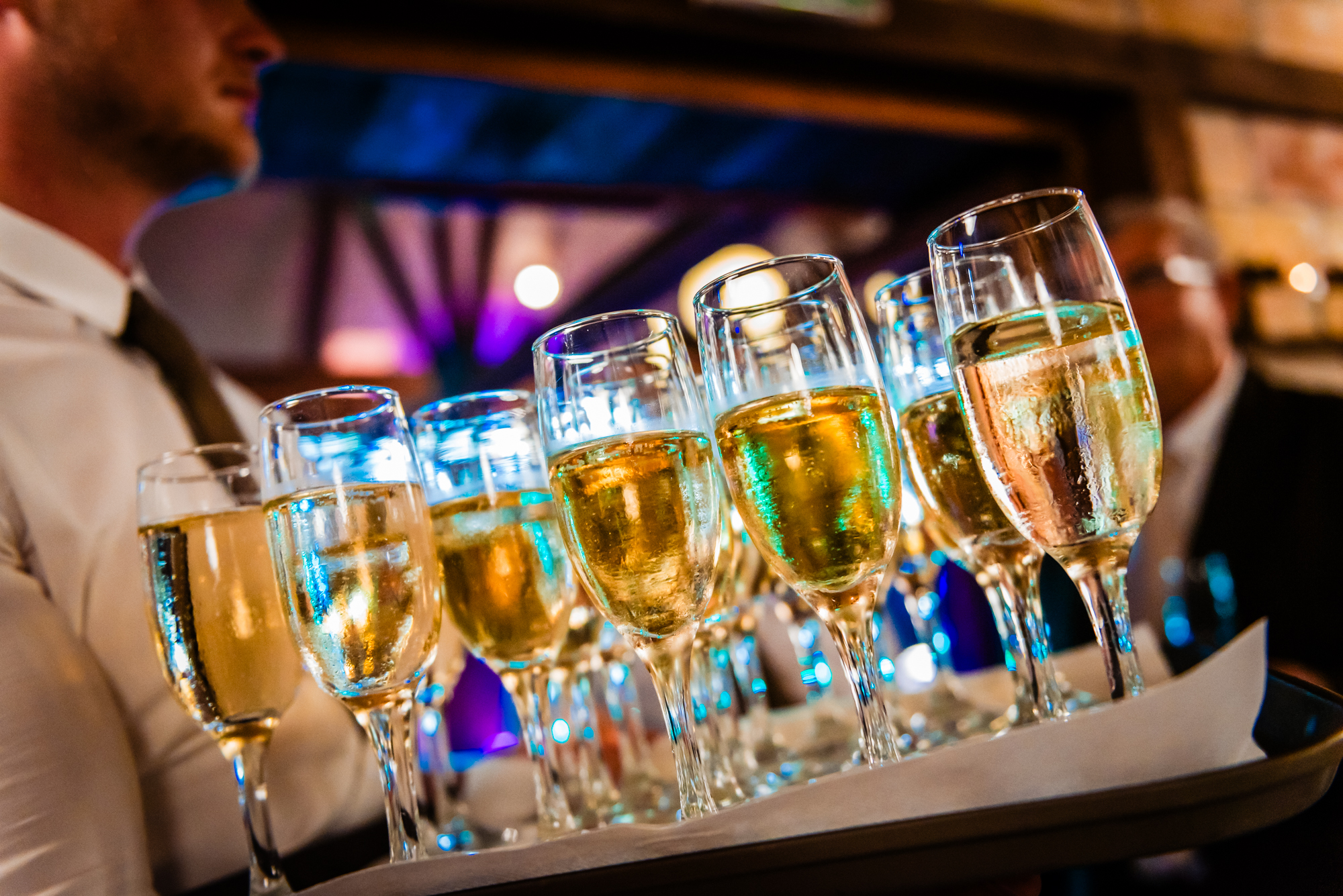Tray of champagne flutes glowing under colourful reception lights during alternative wedding celebration in Budapest.