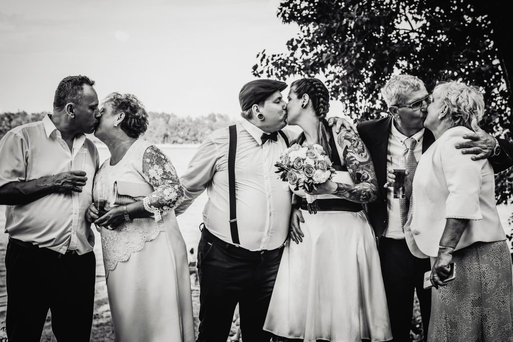 Black and white photo of alternative wedding couple kissing beside their parents outdoors in Budapest.