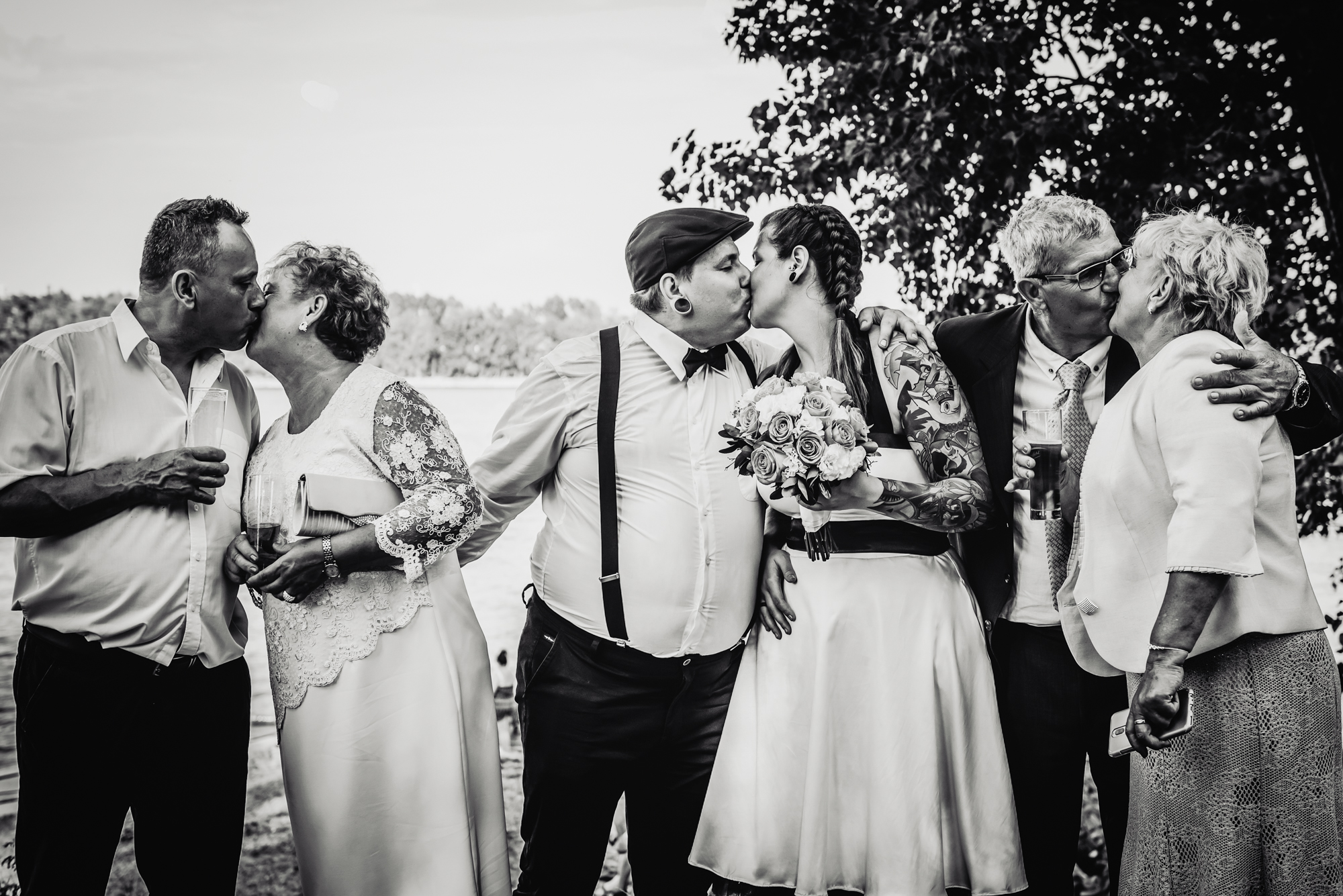 Black and white photo of alternative wedding couple kissing beside their parents outdoors in Budapest.