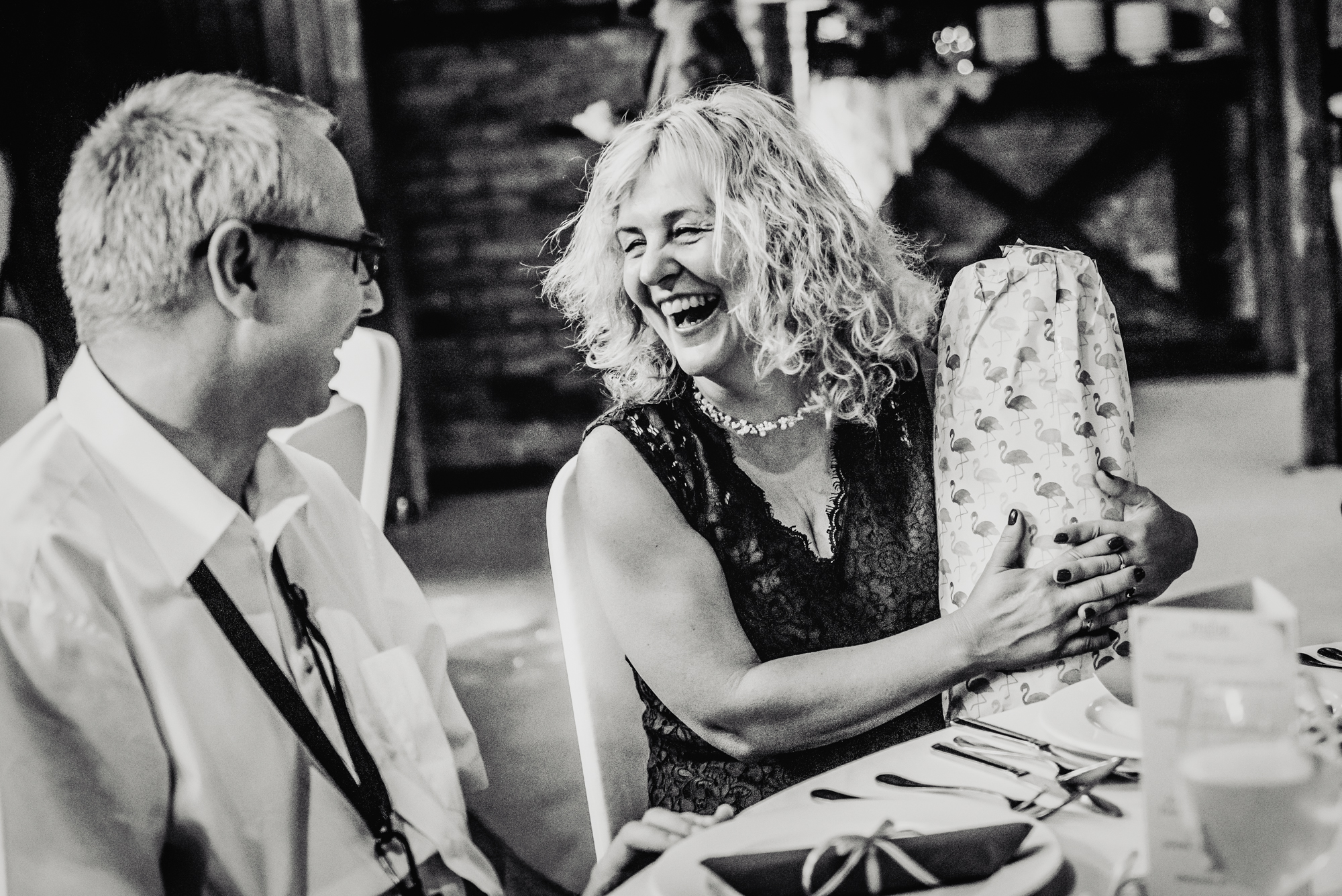 Wedding guest laughing while opening flamingo-patterned gift during alternative wedding reception at Csónakház Budapest.