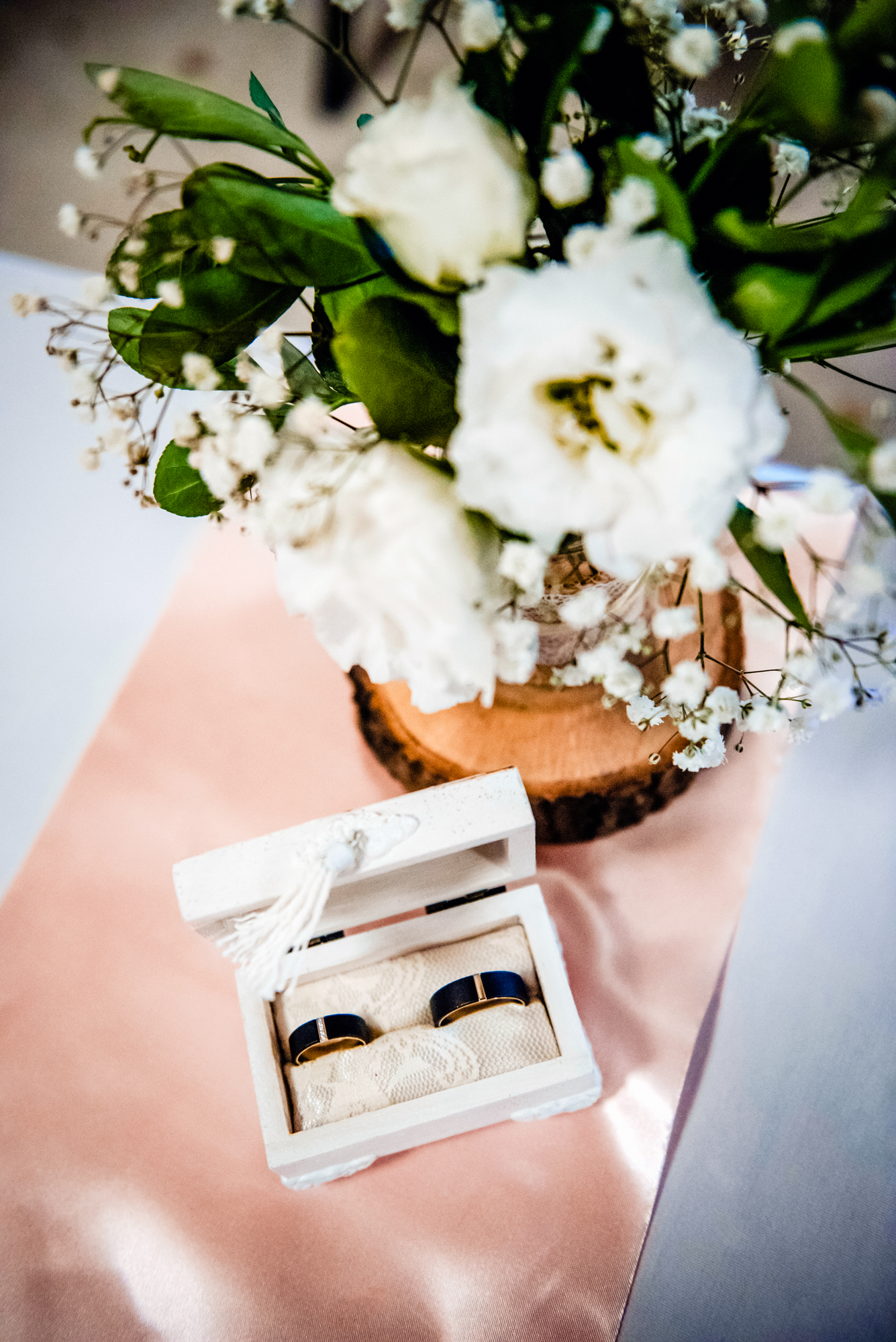 Black and gold wedding bands in an open ring box with soft floral decoration and pastel table styling.