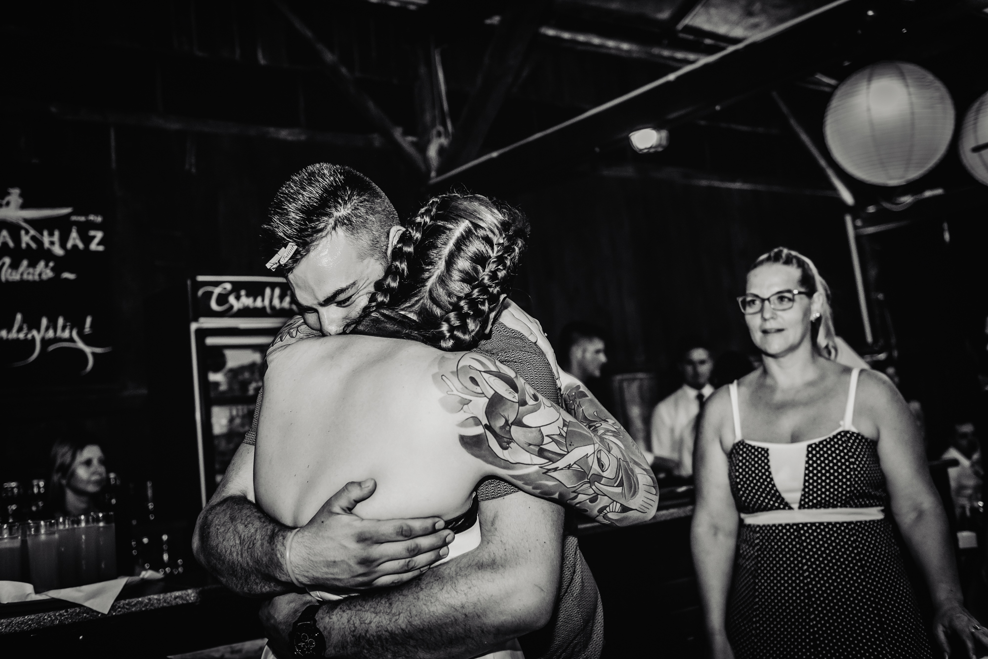 Bride with colourful sleeve tattoos hugging a wedding guest during alternative wedding reception at Csónakház Budapest.