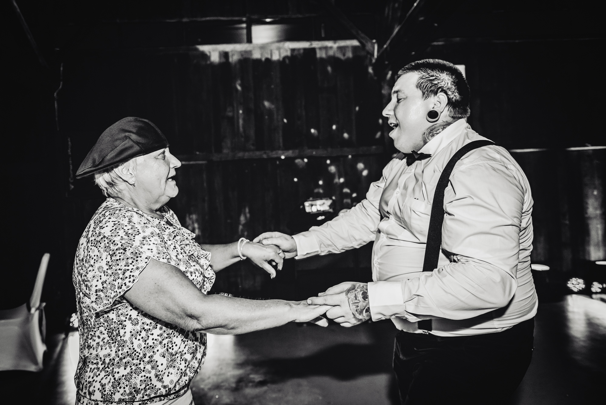 Elderly wedding guest dancing with tattooed guest in suspenders during alternative Budapest wedding celebration.