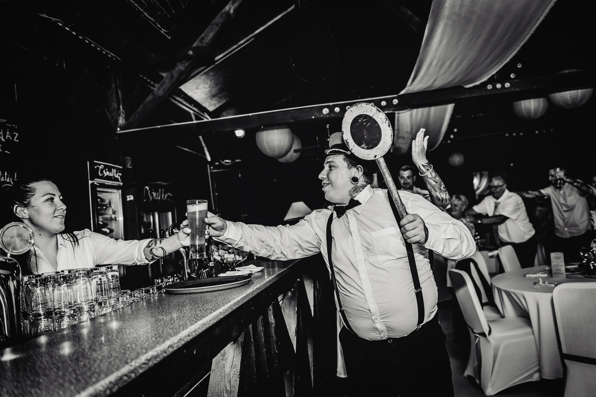 Tattooed groom while cheering with beer at quirky Budapest wedding party.