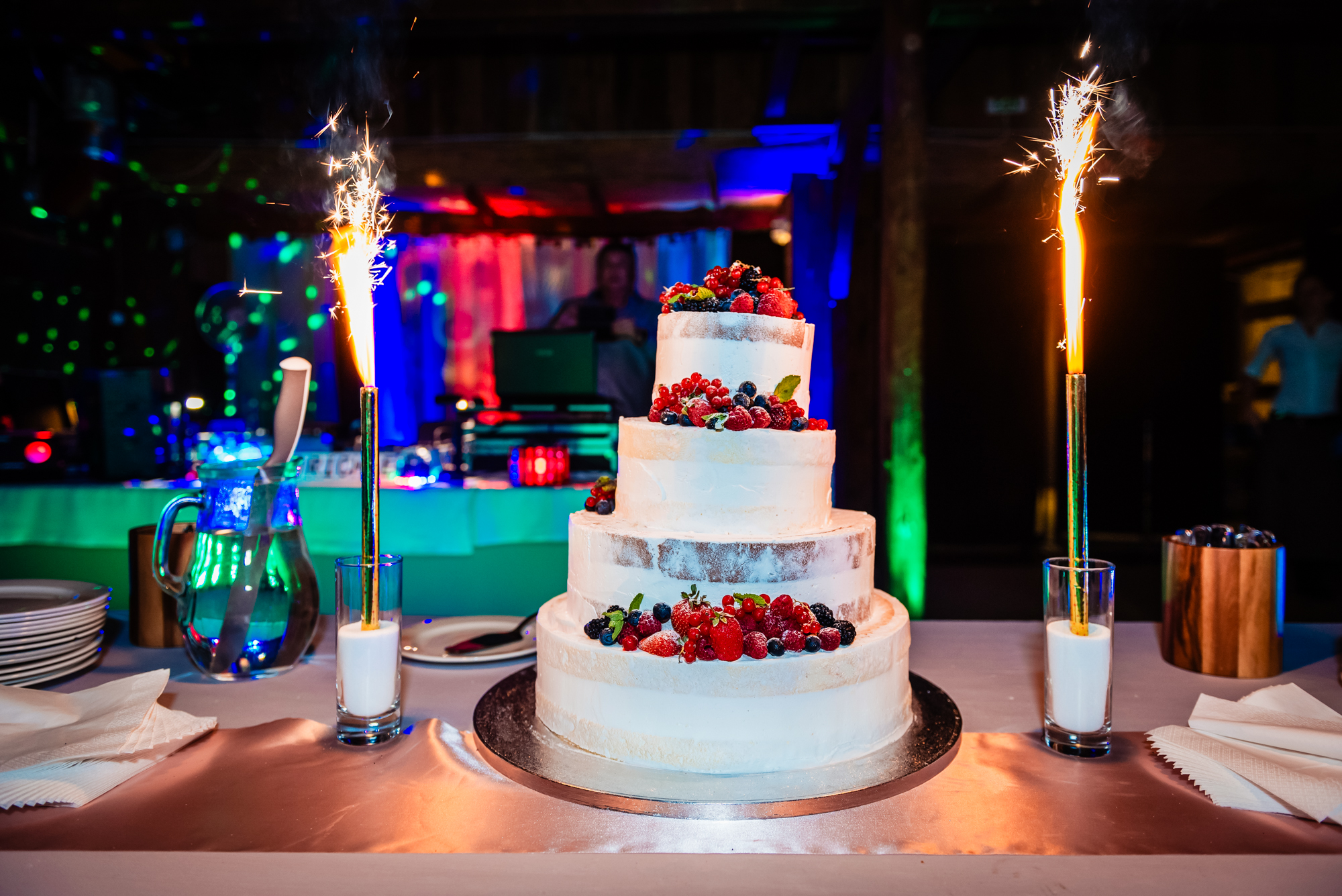 Three-tier wedding cake with fresh berries and sparklers during evening reception at Budapest wedding venue.
