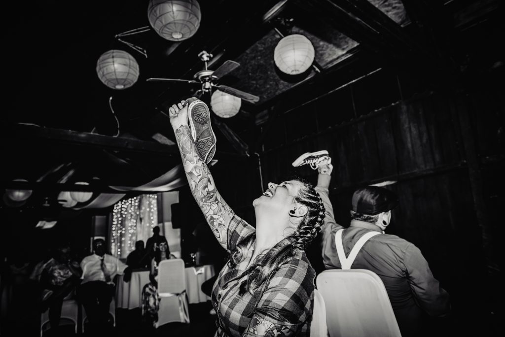 Black and white photo of tattooed bride laughing during wedding shoe game at alternative Budapest wedding.