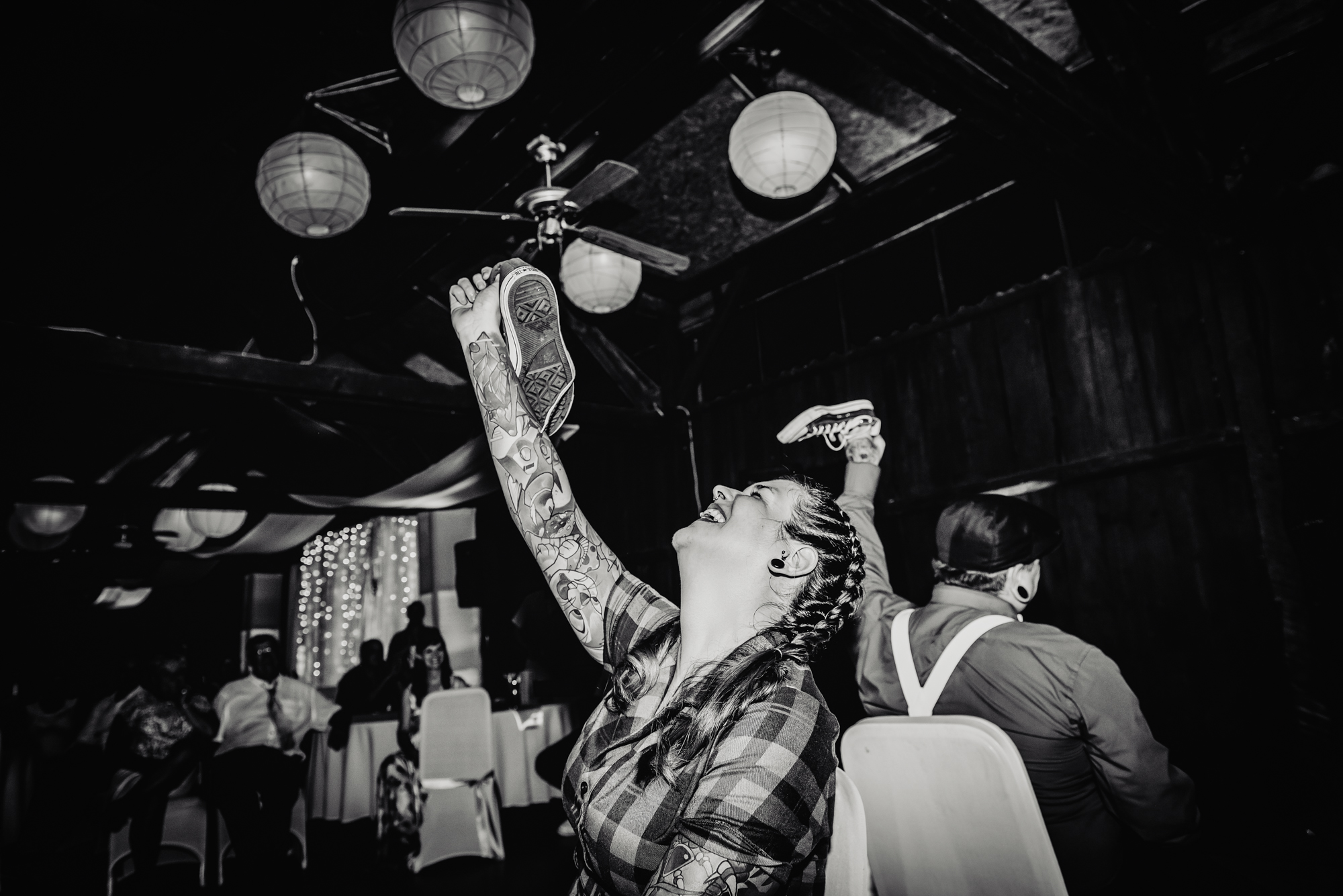 Black and white photo of tattooed bride laughing during wedding shoe game at alternative Budapest wedding.