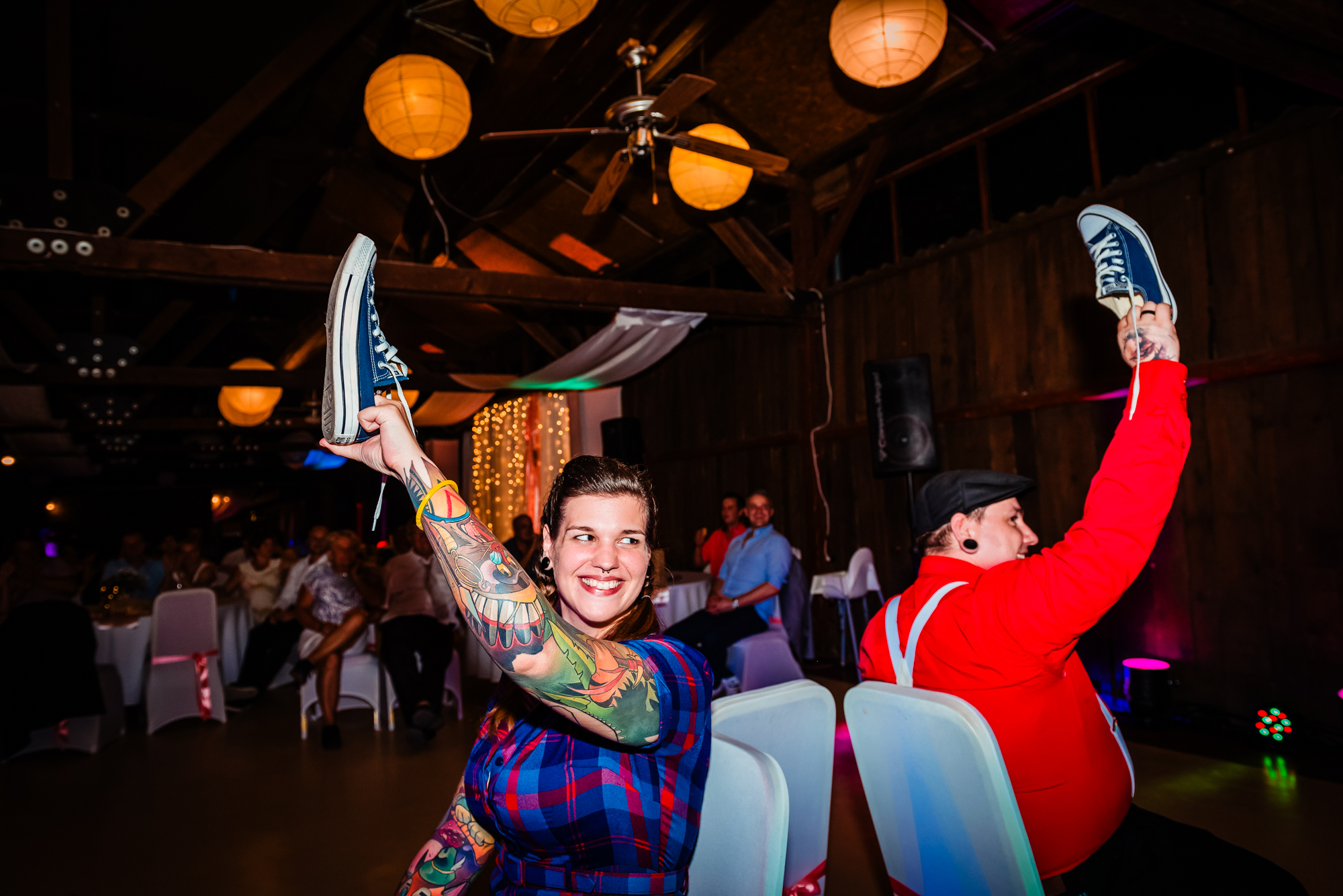 Tattooed bride smiling while holding blue trainer during wedding reception game at Csónakház Budapest.