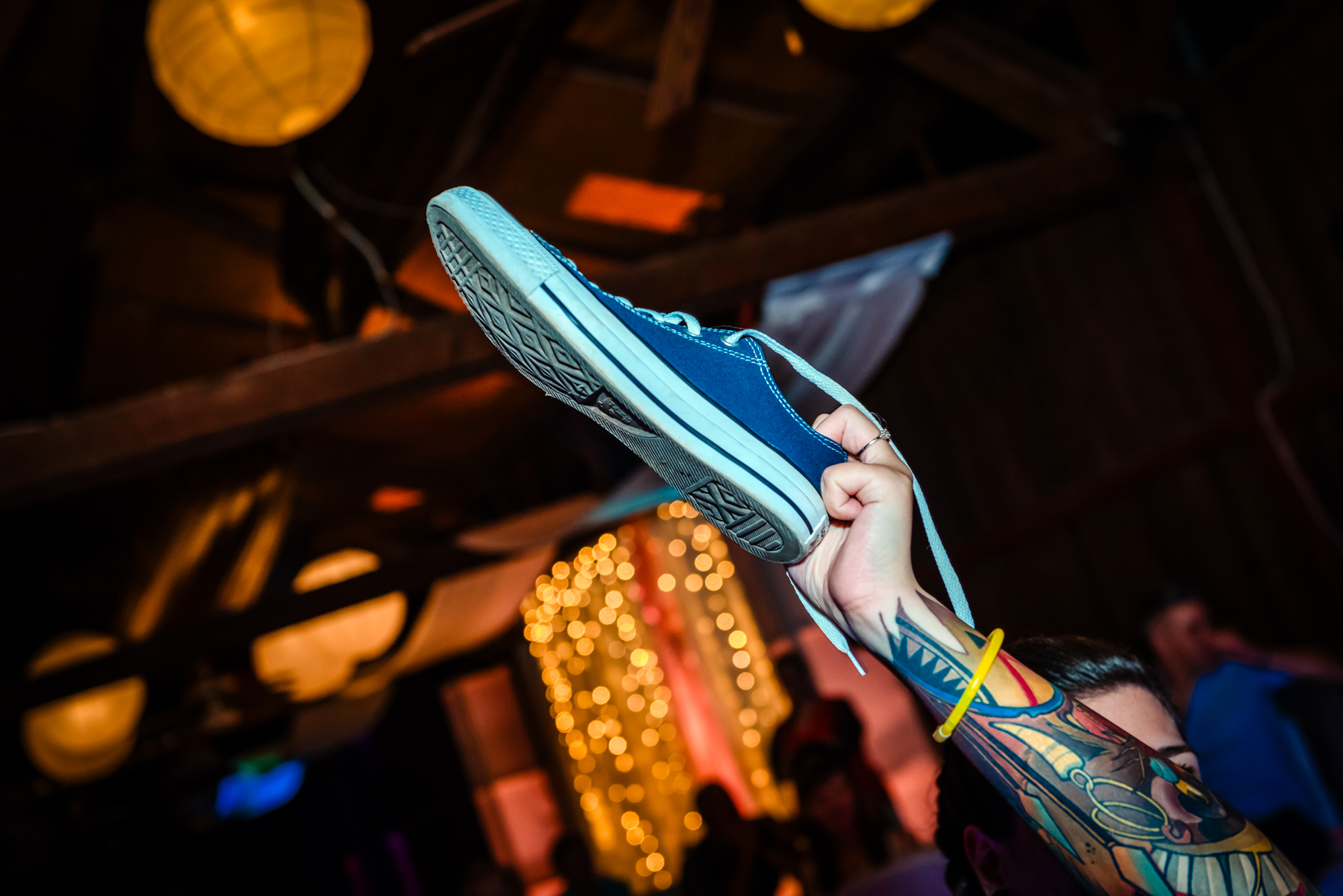 Close-up of tattooed bride raising blue trainer during playful alternative wedding reception game in Budapest.