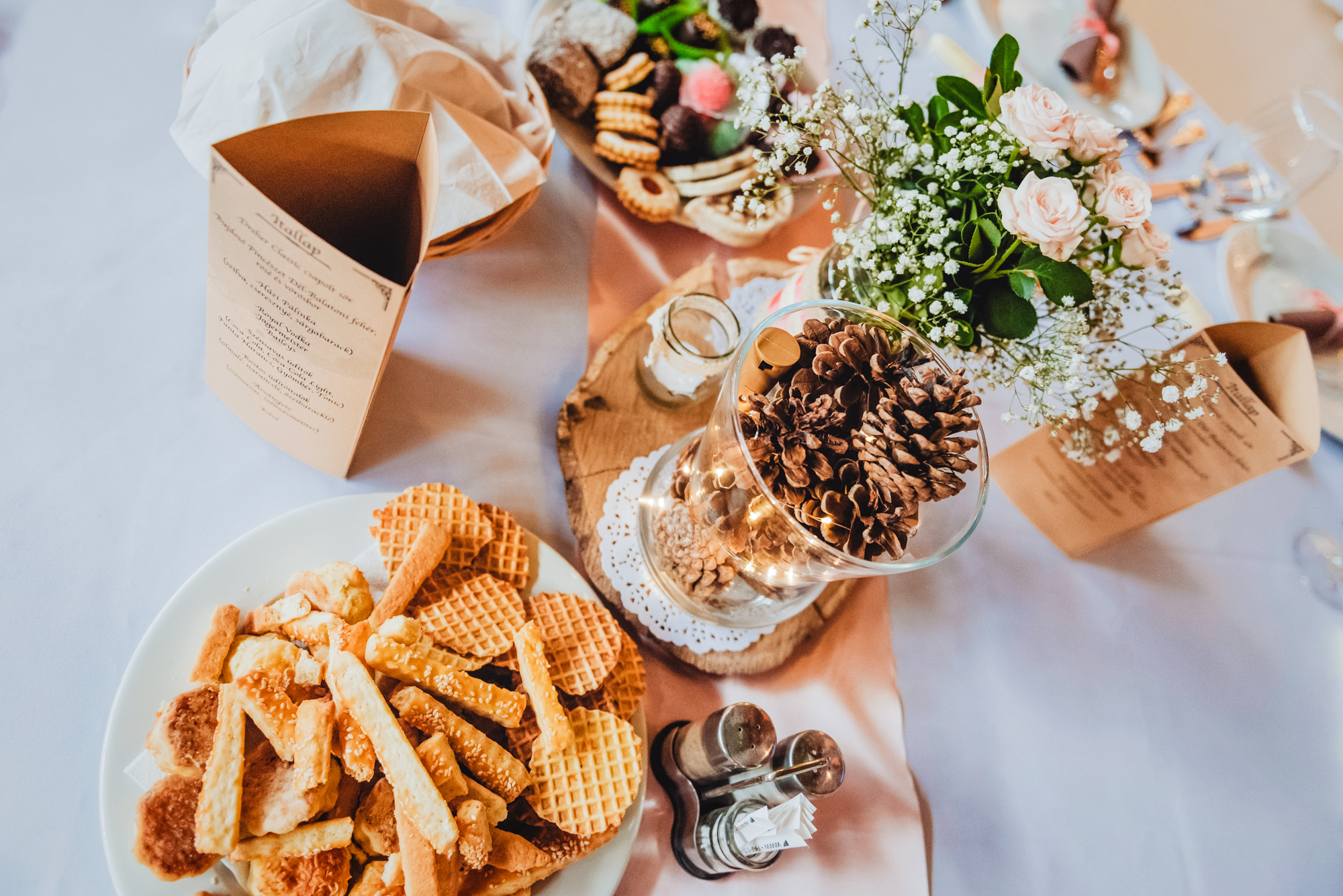 Wedding reception table with pastries, pinecone centrepiece, flowers, and printed menus at Budapest wedding venue.