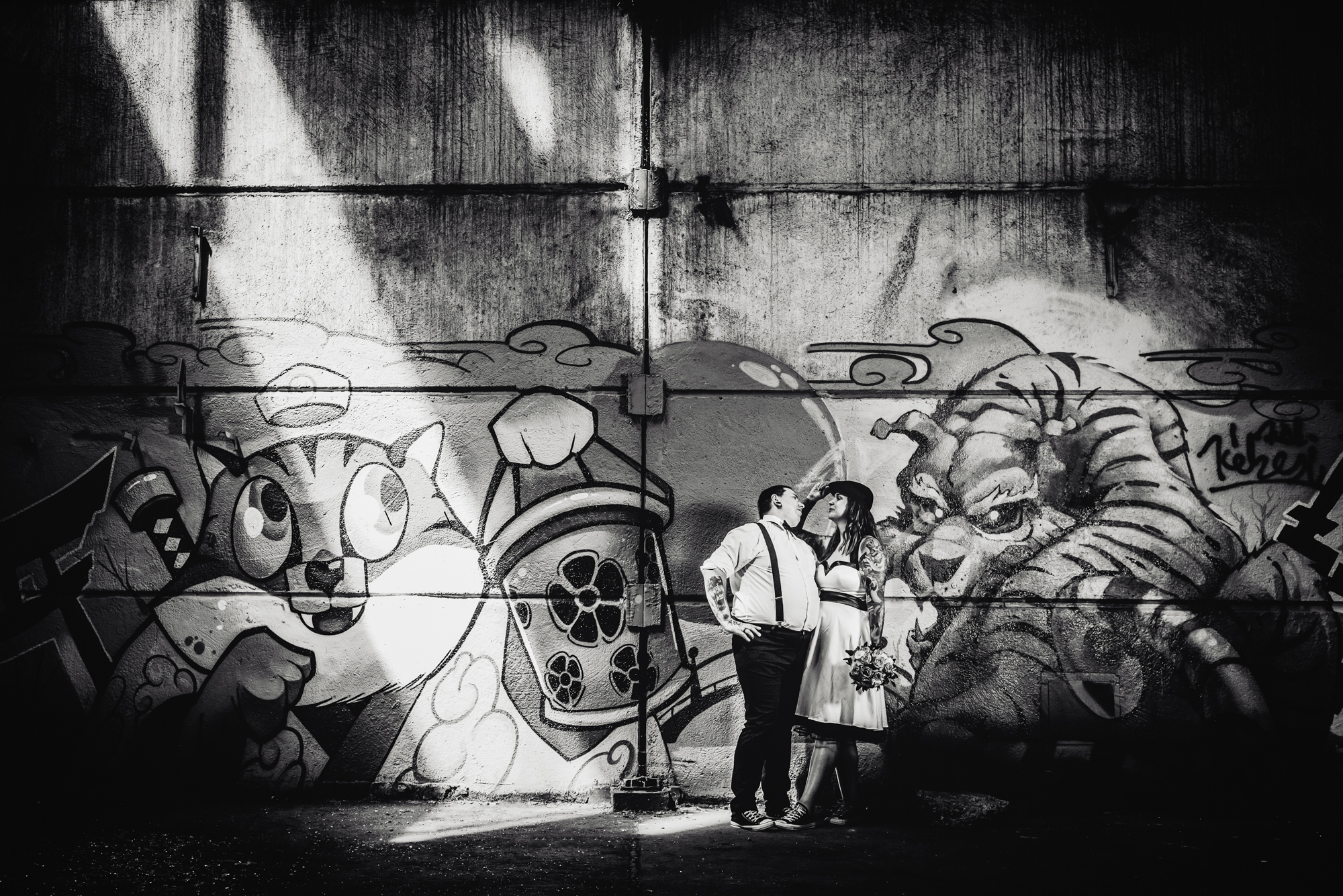 Alternative wedding couple standing beneath colourful graffiti artwork inside an abandoned Budapest warehouse.