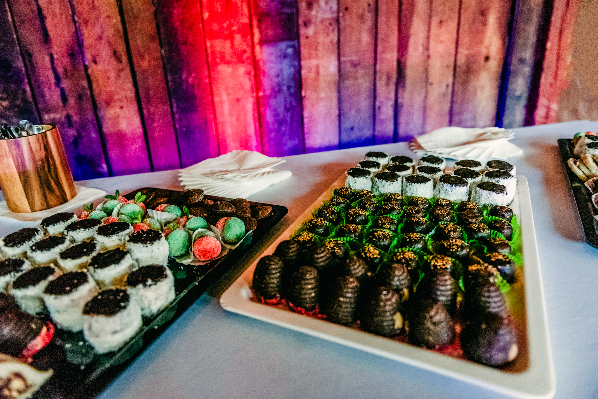 Assorted wedding desserts and sweets displayed on reception table with colourful ambient lighting.