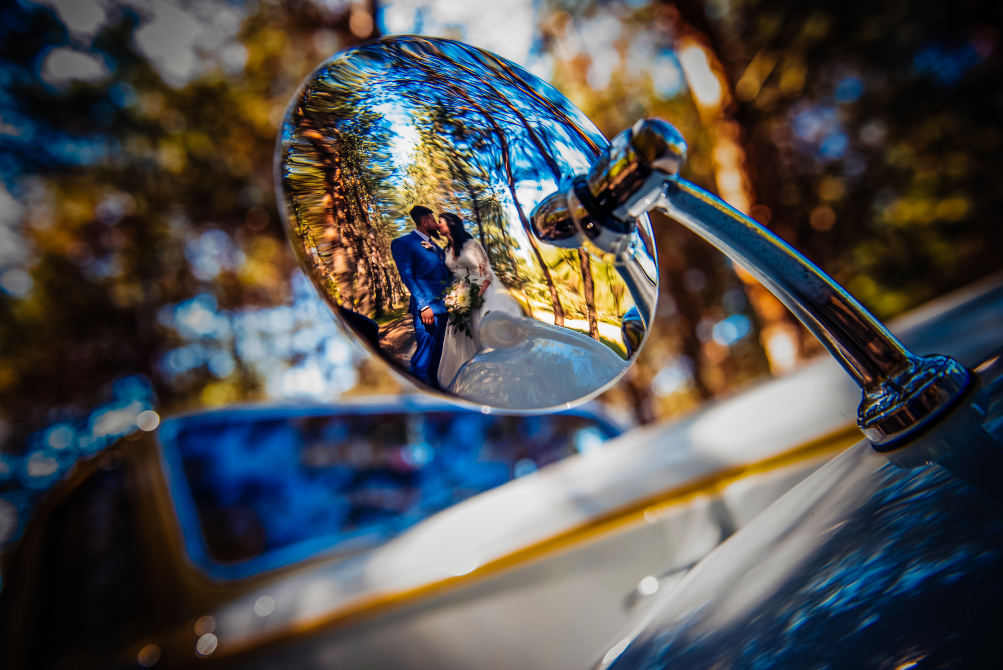 Bride and groom reflected in a vintage car mirror during creative wedding portraits.