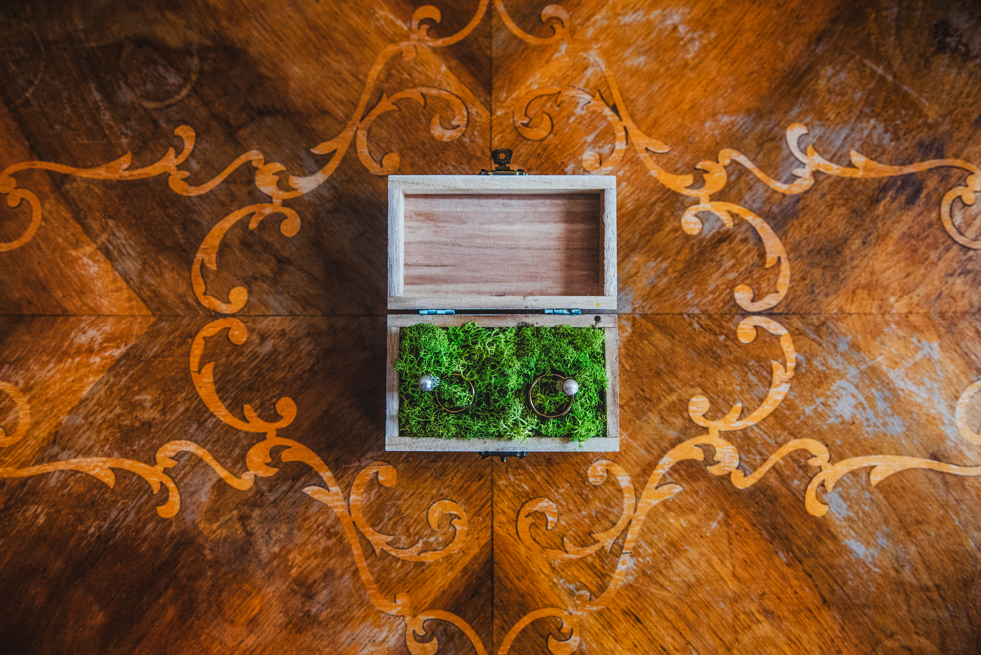 Wedding rings resting in a moss-filled wooden box on an ornate wooden table at Bodrogi Kuria Wellness Hotel.