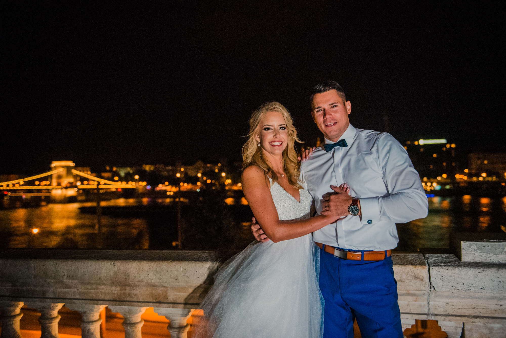 Bride and groom posing on terrace overlooking Chain Bridge during Budapest wedding night portraits.