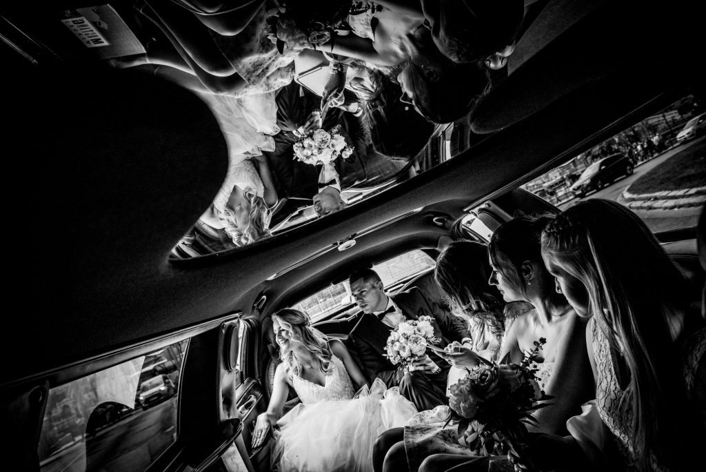 Black and white limousine photo of bride, groom, and bridesmaids travelling through Budapest.