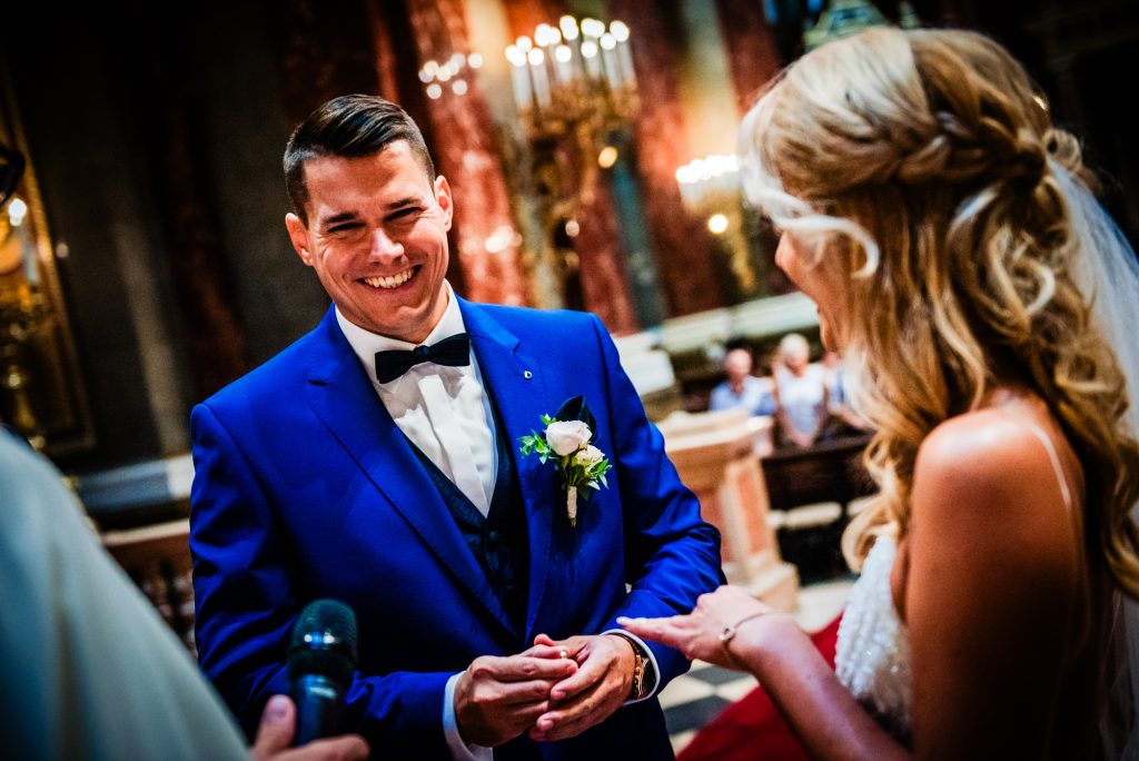 Groom smiling while placing wedding ring on bride’s hand during Budapest church ceremony.