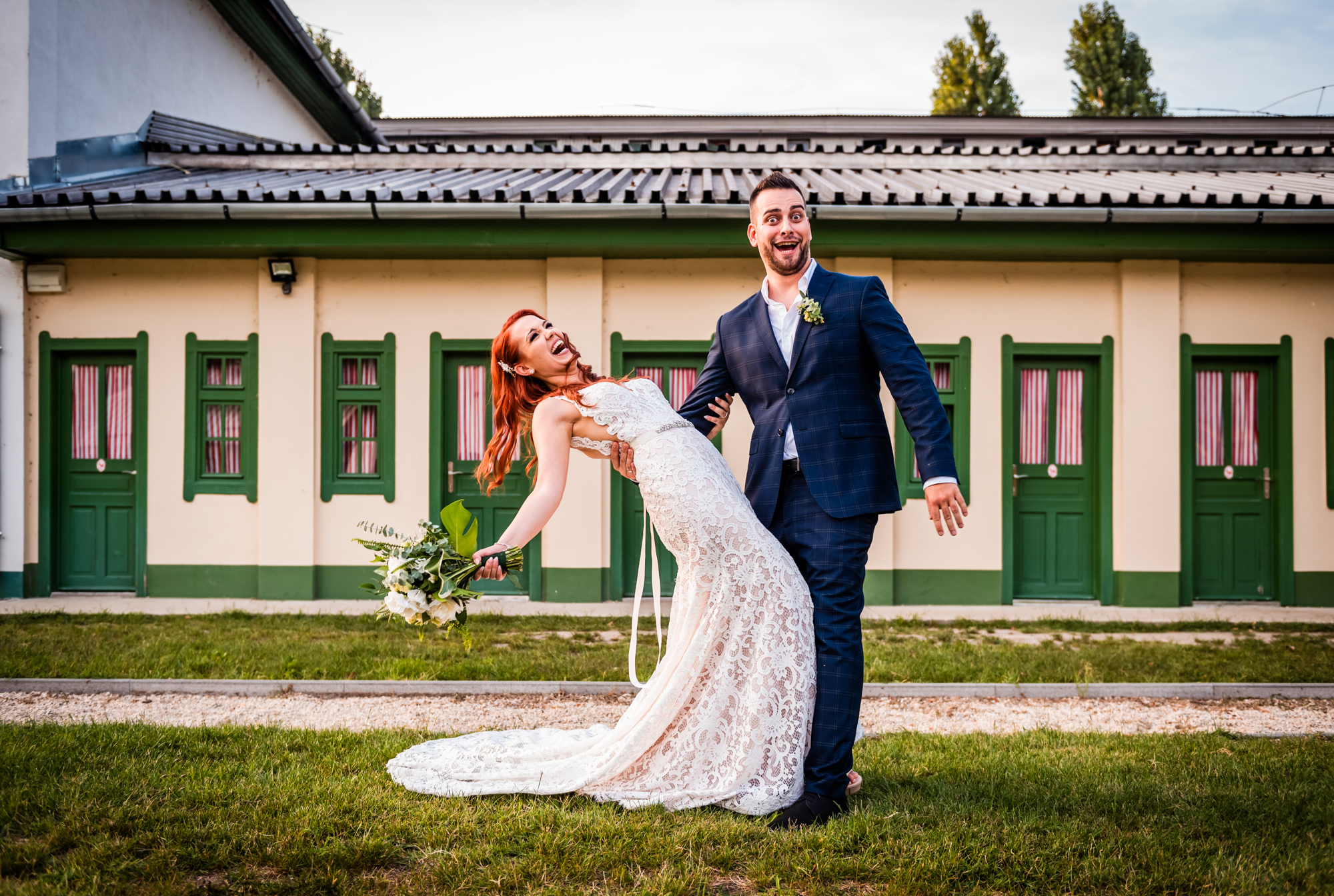 Groom reacts with surprise as the laughing bride dips backwards holding her bouquet.